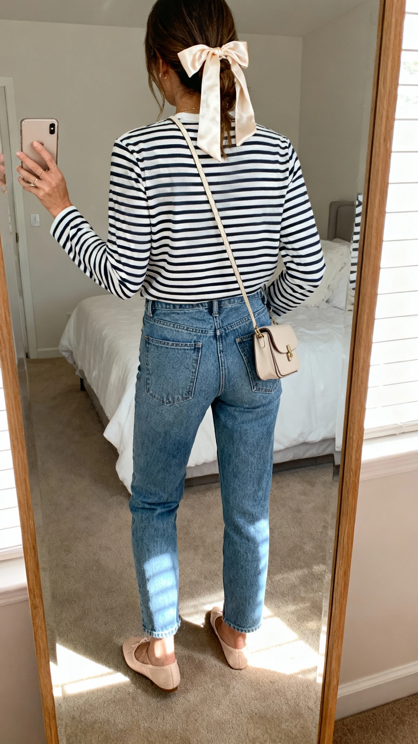 iPhone back view of a woman wearing mom jeans, a classic Breton striped long-sleeve tee, ballet flats, a small crossbody, and a silk hair ribbon, face not visible, bedroom mirror with soft daylight, iPhone photo quality.