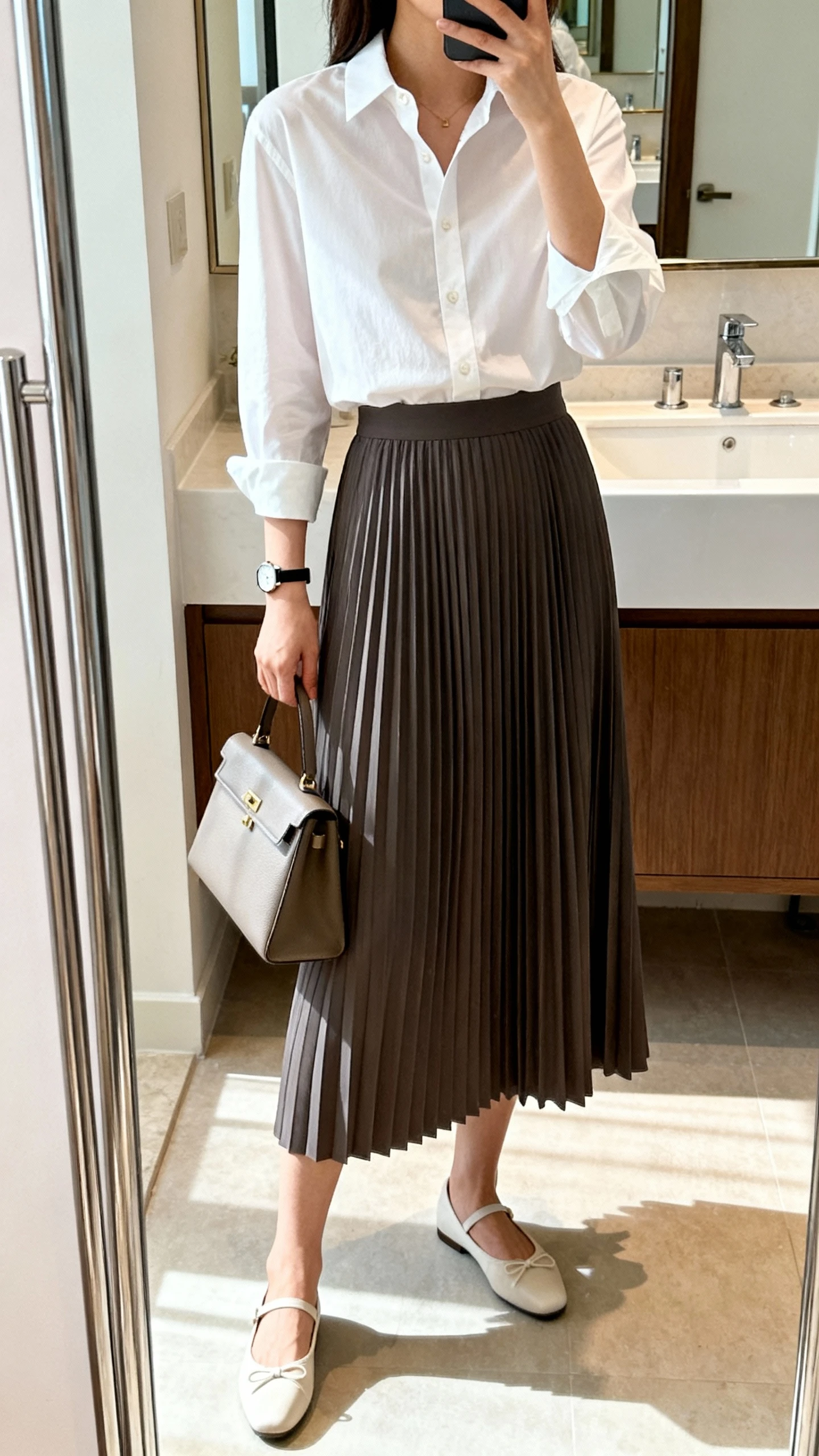 iPhone mirror selfie of a woman in a crisp white button-down tucked into a pleated midi skirt, classic ballet flats, structured handbag, and a slim watch, face not visible, cropped at neck, bathroom mirror, bright indoor light, iPhone photo quality.
