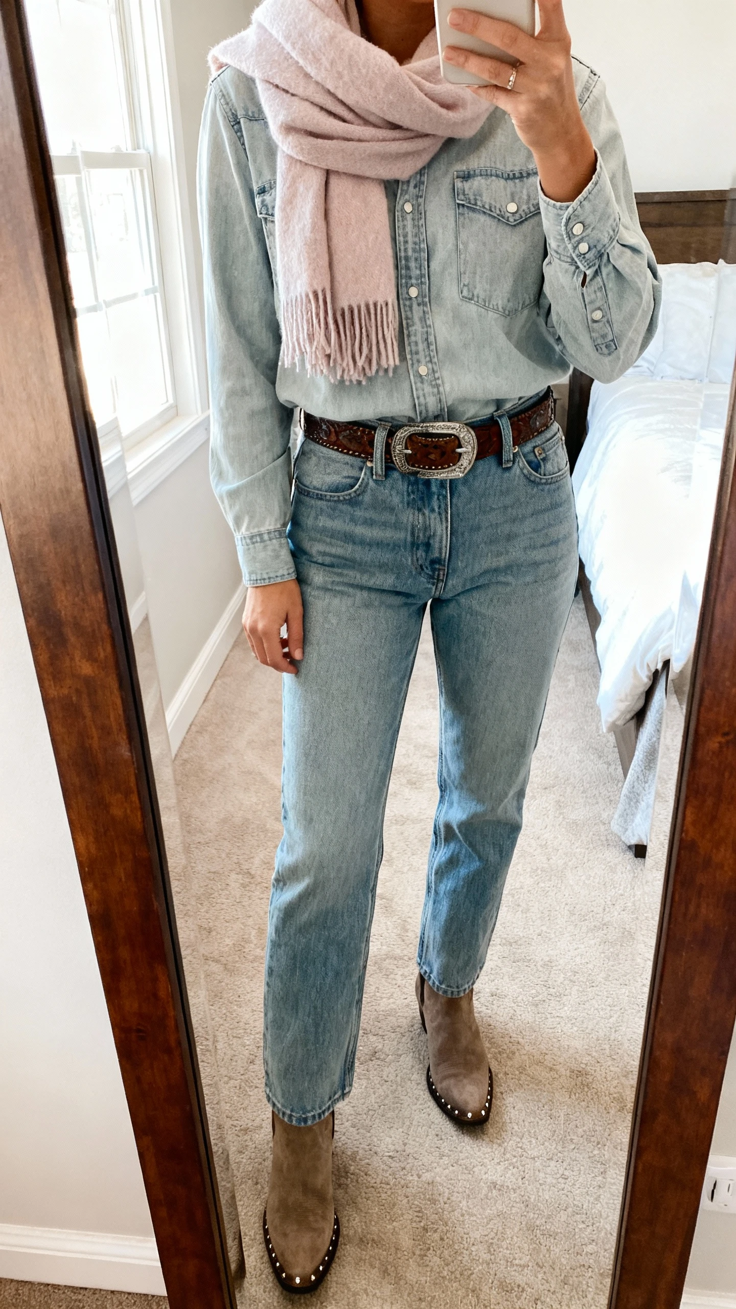 iPhone mirror selfie of a woman in a light-wash denim shirt tucked into matching high-rise straight jeans with a soft pastel cashmere scarf, western belt, ankle boots, minimal studs, face not visible, cropped at shoulders, bedroom mirror, natural daylight, iPhone photo quality.