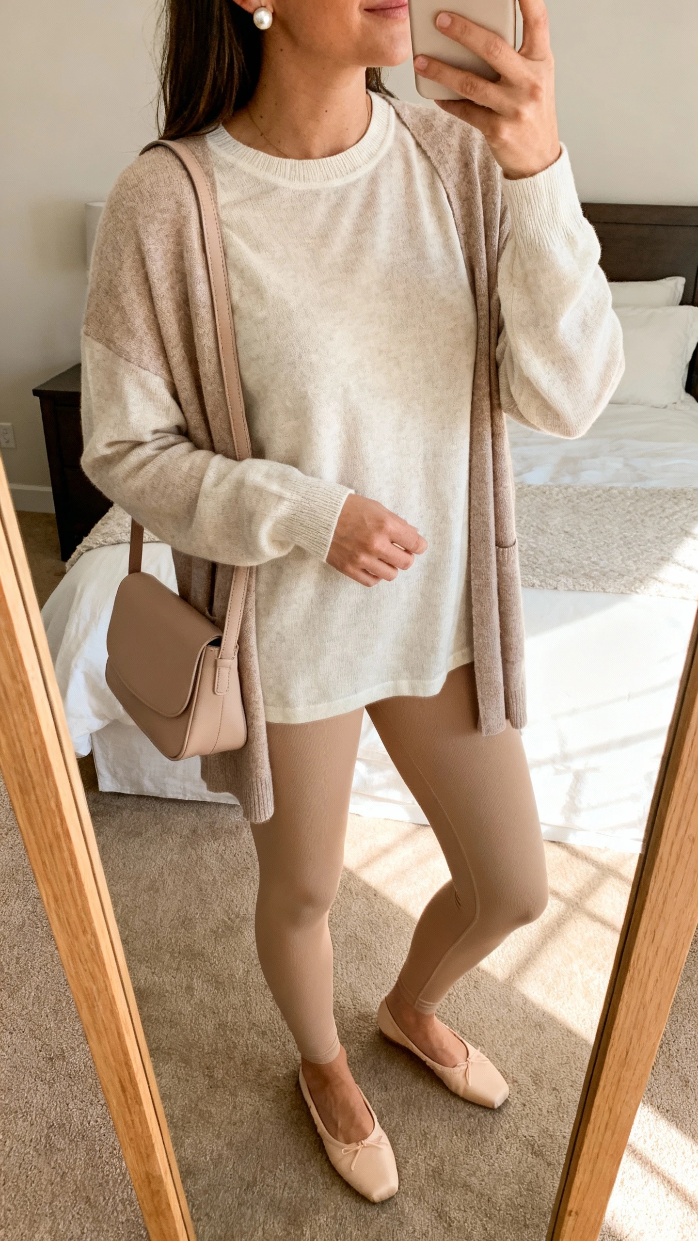 iPhone mirror selfie of a woman in a lightweight cotton crewneck sweater with a coordinating cardigan, seamless leggings in sand, minimal ballet flats, a soft shoulder bag in matching neutral, pearl stud earrings, face not visible, cropped at neck, bedroom mirror, warm afternoon light, iPhone photo quality.