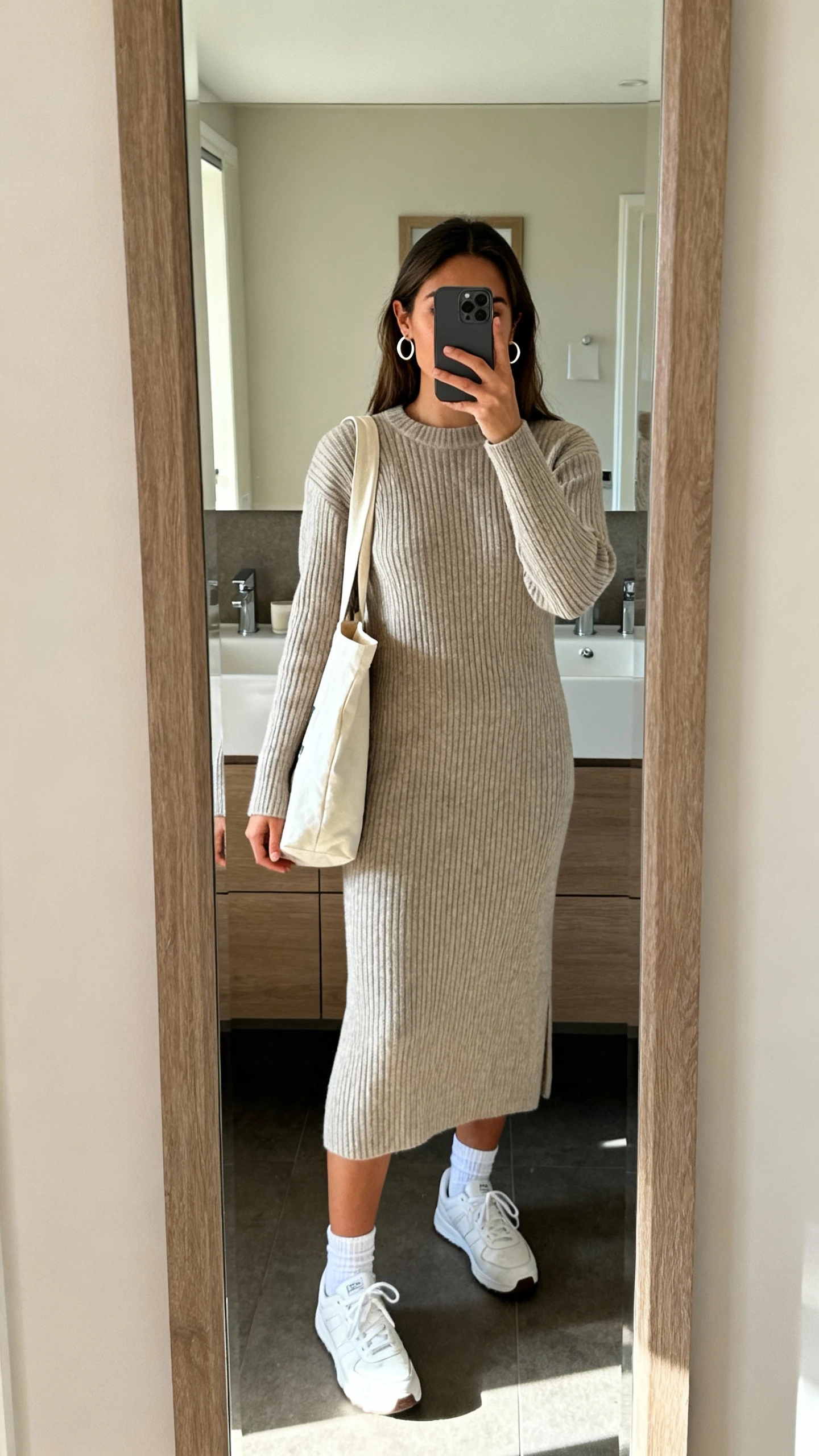 iPhone mirror selfie of a woman in a ribbed sweater dress with classic white sneakers and ankle socks, simple hoop earrings, and a tote bag, face not visible, bathroom full-length mirror, soft morning light, iPhone photo quality.