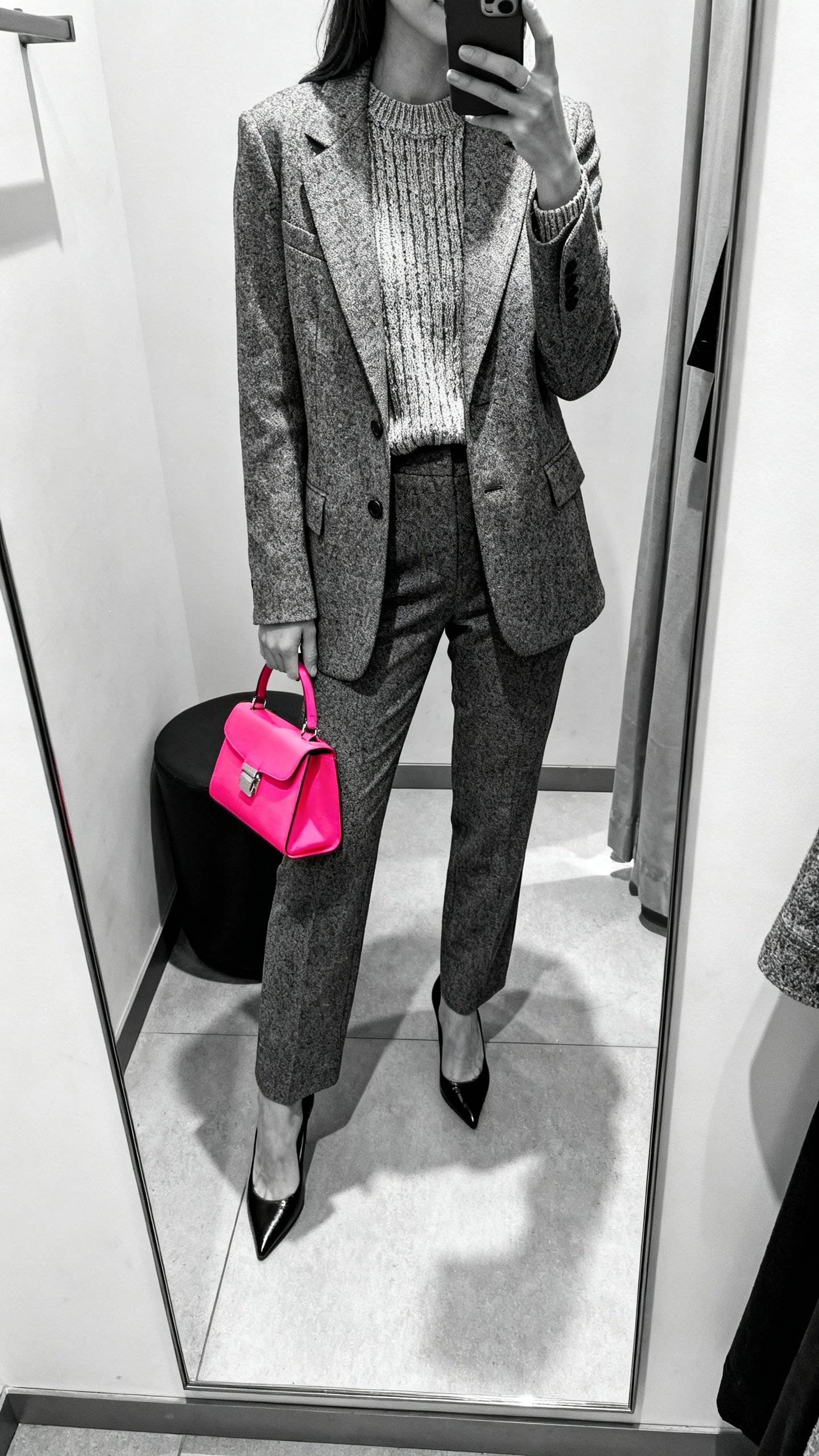 iPhone mirror selfie of a woman in tonal layers: monochrome knit top, matching blazer, coordinating trousers, with a bright pop-color bag and heels, face not visible, cropped at shoulders, dressing-room mirror, indoor lighting, iPhone photo quality.
