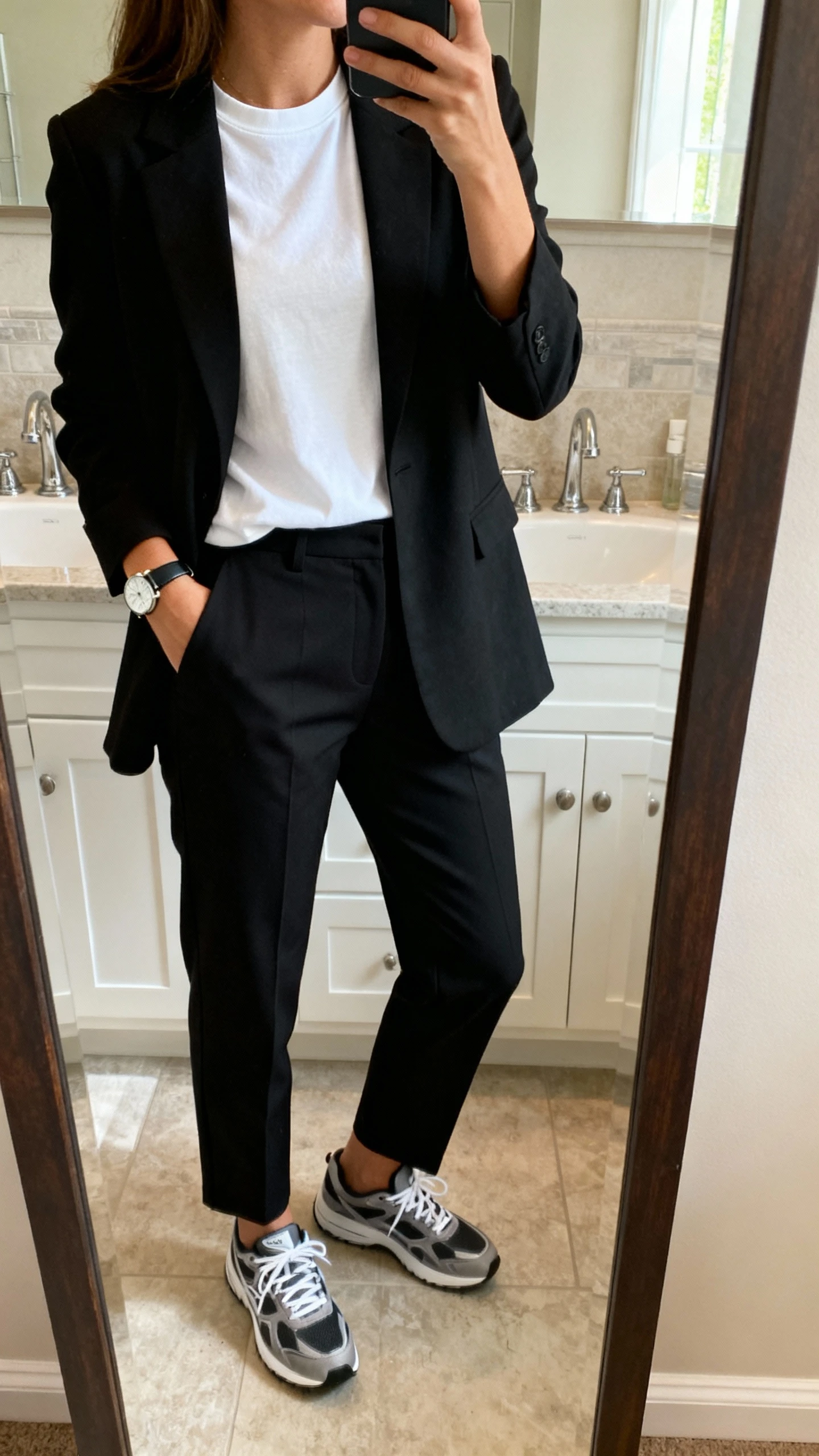 iPhone mirror selfie of a woman wearing a black blazer over a white crewneck tee with tailored black trousers, sleek sneakers, simple watch, face not visible, bathroom full-length mirror, soft indoor morning light, iPhone photo quality