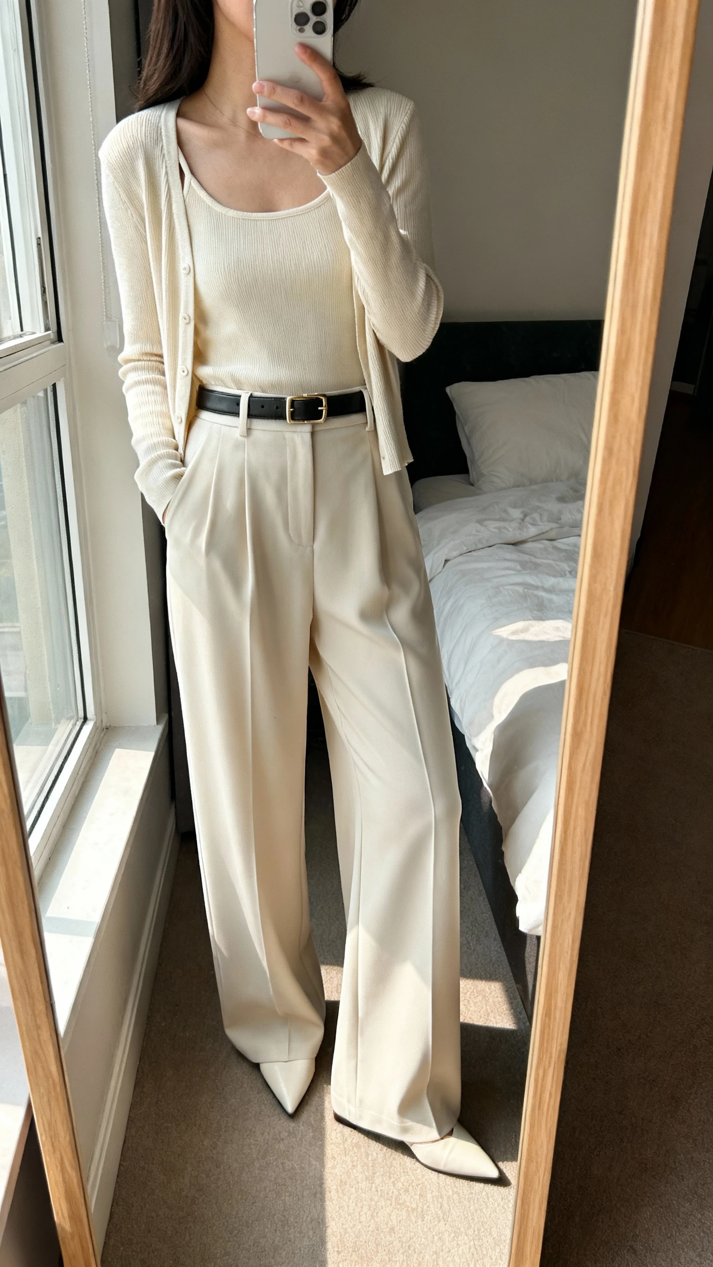 iPhone mirror selfie of a woman wearing a cardigan-and-tank matching set with high-waisted wide-leg trousers, sleek belt, and pointed flats, face not visible, side angle, full-length mirror in bedroom, natural window light, iPhone photo quality.