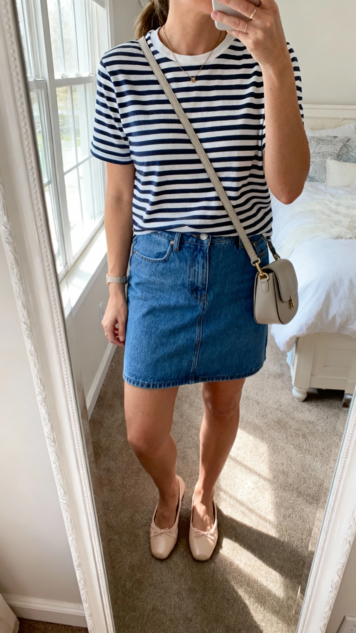 iPhone mirror selfie of a woman wearing a classic navy-and-white striped tee, blue denim mini skirt, and ballet flats with a simple crossbody bag, face not visible, cropped at neck, bedroom mirror, natural window light, iPhone photo quality.