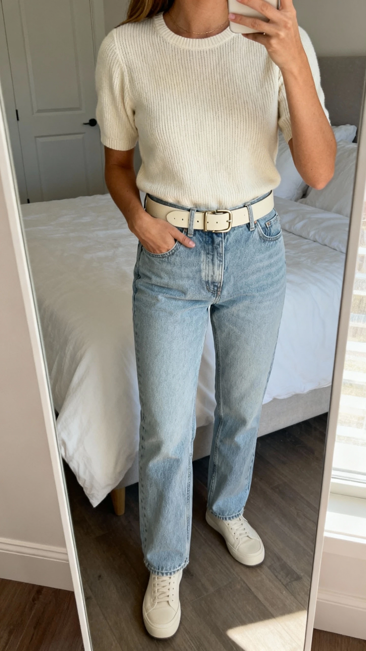 iPhone mirror selfie of a woman wearing a monochrome look: mom jeans and a matching tonal knit top with same-color belt and minimal sneakers, face not visible, cropped at neck, bedroom mirror, natural morning light, iPhone photo quality.
