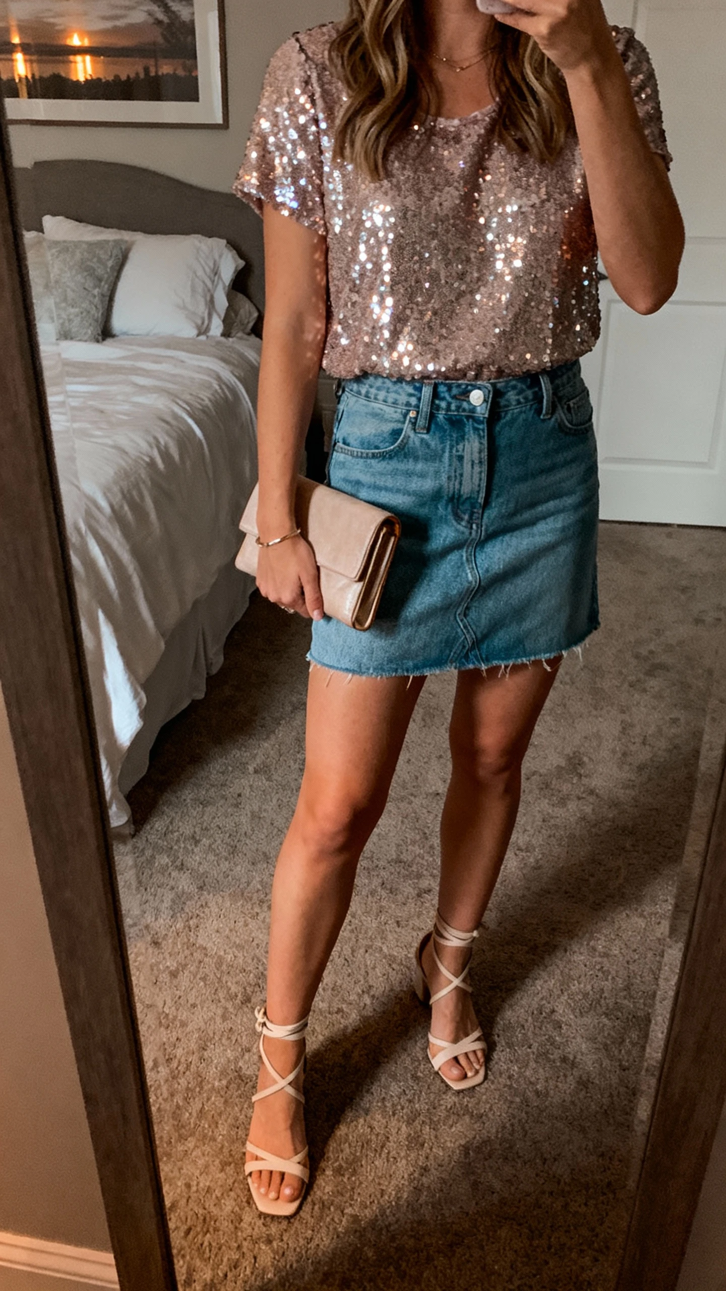 iPhone mirror selfie of a woman wearing a sequin top with a denim mini skirt, strappy heels, and a clutch, face not visible, cropped at shoulders, bedroom mirror, evening indoor lighting, iPhone photo quality.