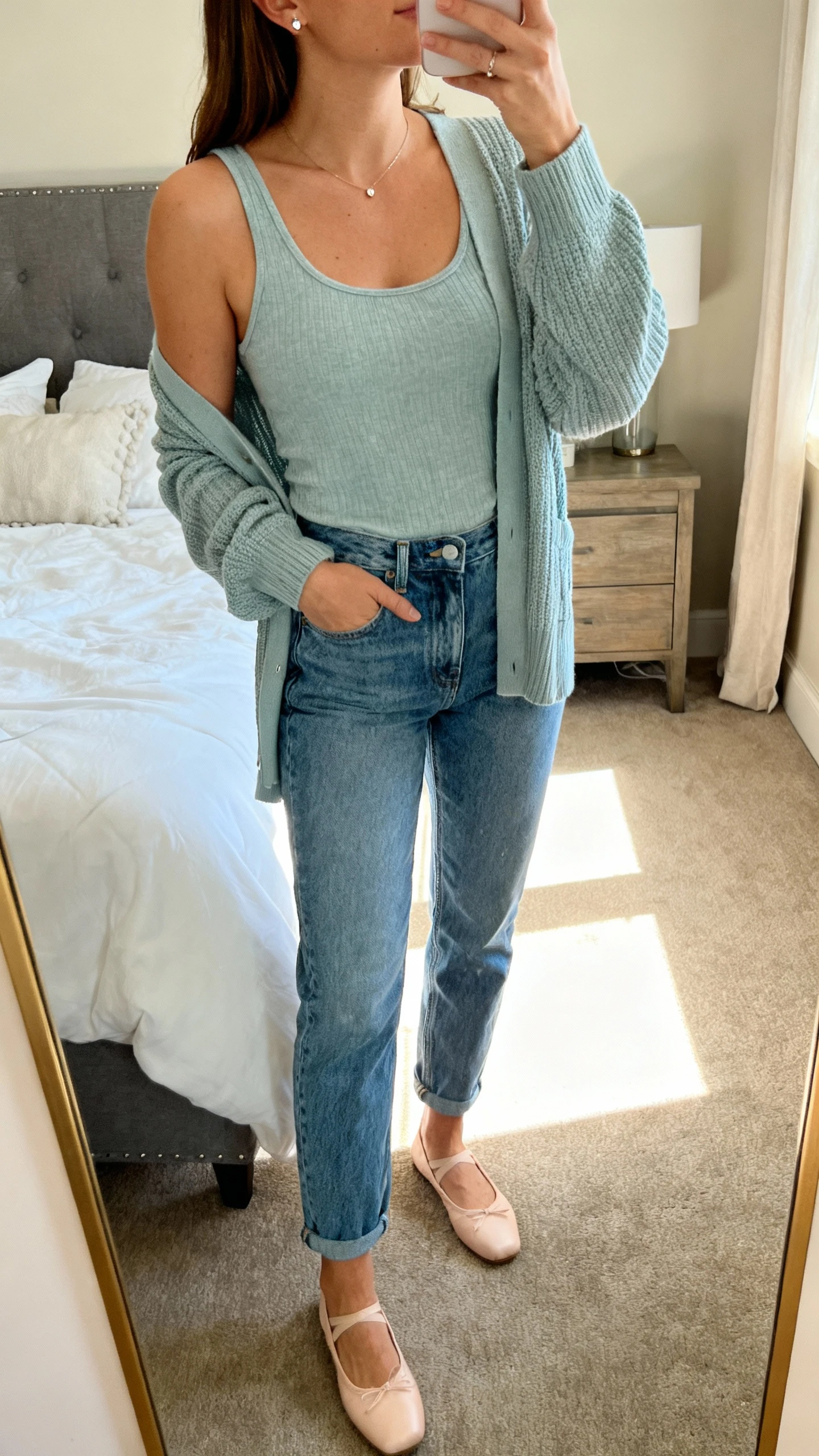iPhone mirror selfie of a woman wearing mom jeans and a matching cardigan set (tank + cardigan), ballet flats, dainty studs, face not visible, cropped at neck, cozy bedroom mirror with morning light, iPhone photo quality