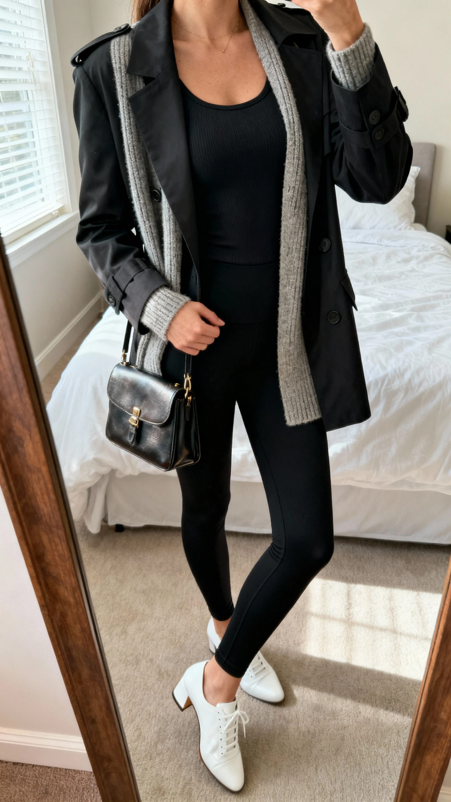 iPhone mirror selfie of a woman wearing sleek black leggings styled three ways: swap between blazer, trench, or knit cardigan layered over a fitted tank, with white sneakers or heels and a small leather bag, face not visible, cropped at neck, bedroom mirror, natural window light, iPhone photo quality.
