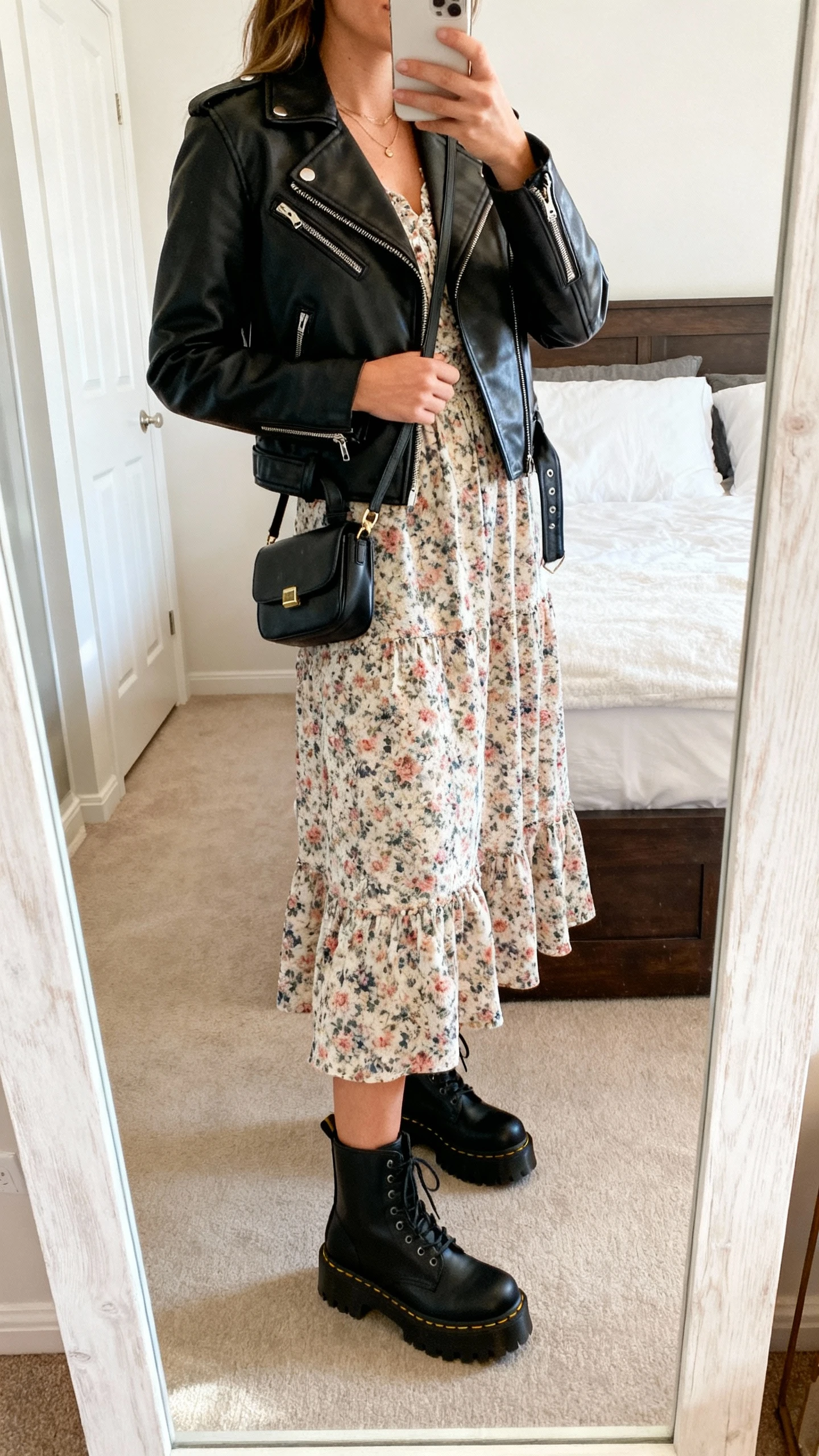iPhone side-angle mirror selfie of a woman in a floral romantic midi dress with a leather moto jacket and chunky black combat boots, small crossbody bag, face not visible, cropped at shoulders, bedroom mirror with natural daylight, iPhone photo quality.