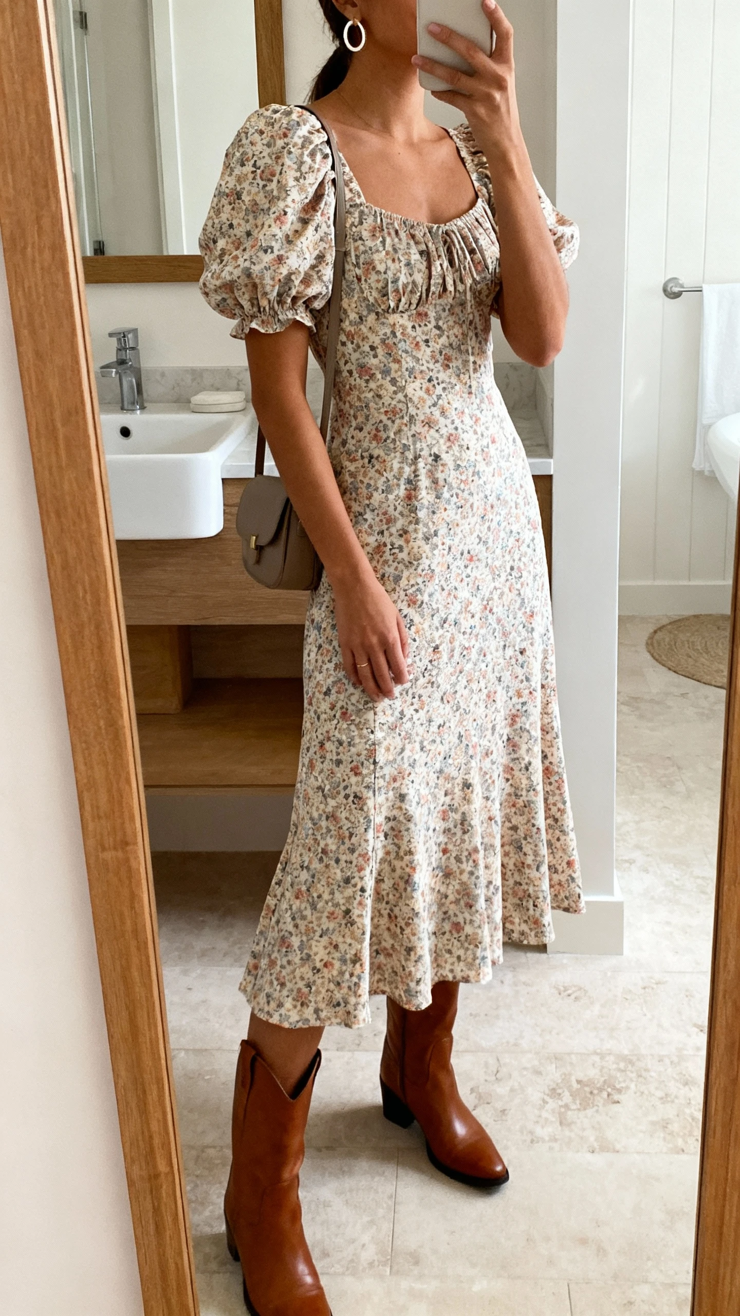 iPhone side-angle mirror selfie of a woman in a romantic puff-sleeve midi dress with a floral print, mid-calf leather boots, simple hoop earrings, and a small shoulder bag, face not visible, bathroom mirror, soft indoor light, iPhone photo quality.