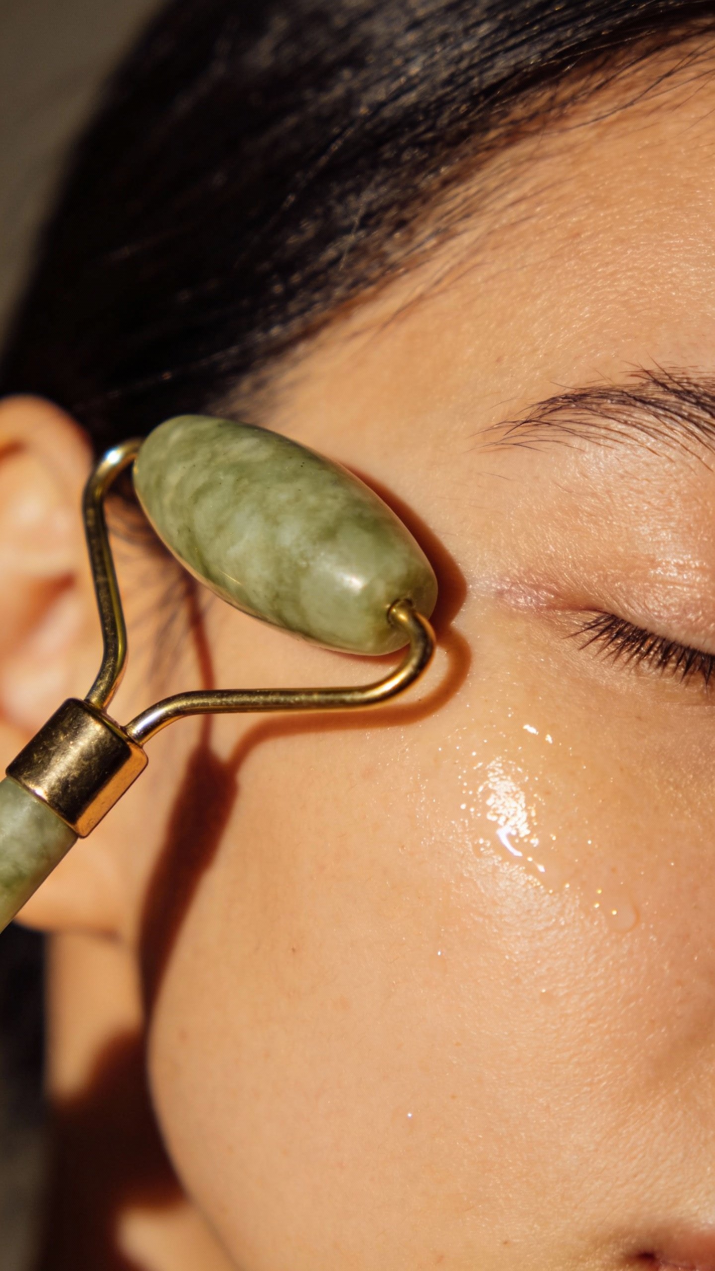 single jade roller gliding on dewy cheekbone, studio light