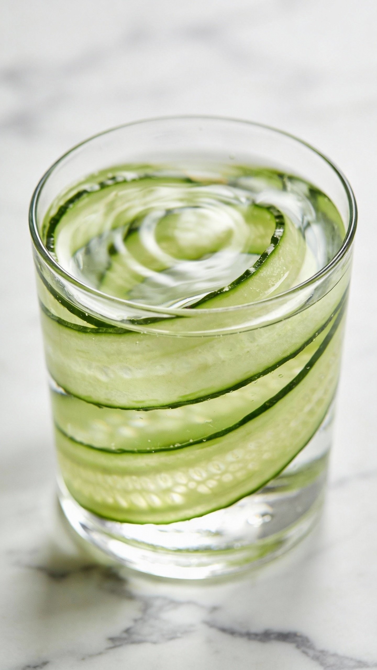 glass of cucumber-infused water on white marble closeup