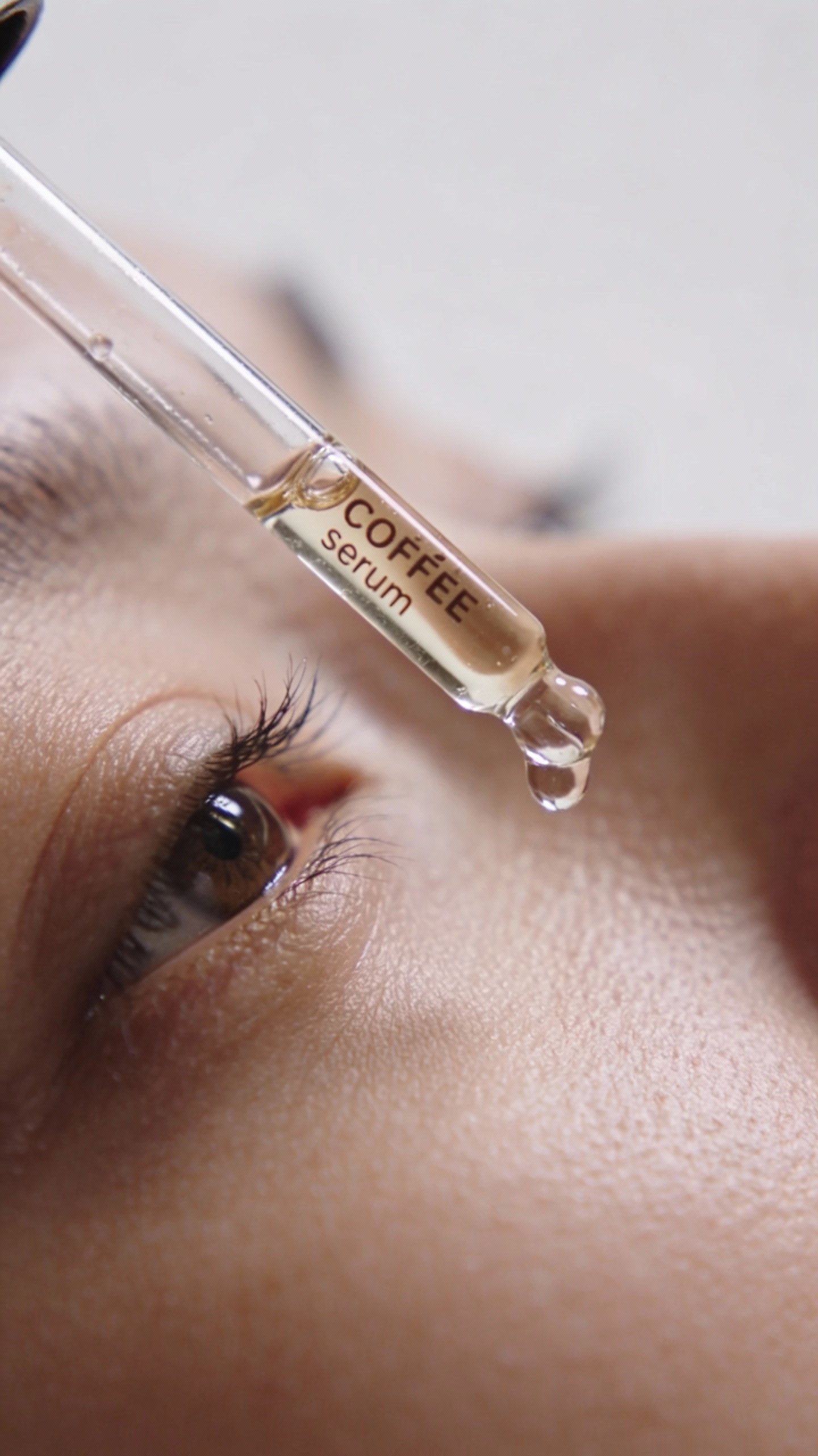 closeup of caffeine eye serum dropper above under-eye skin