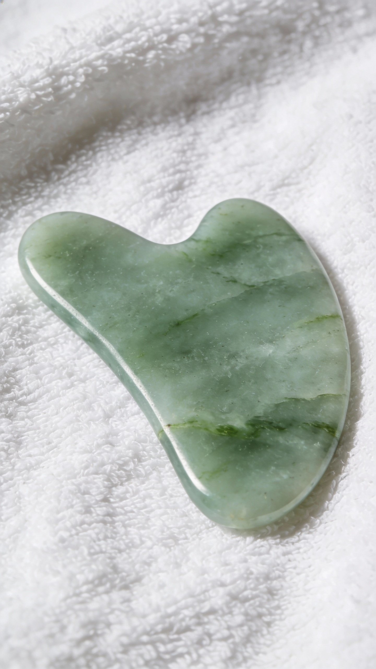 jade gua sha stone on clean white towel closeup