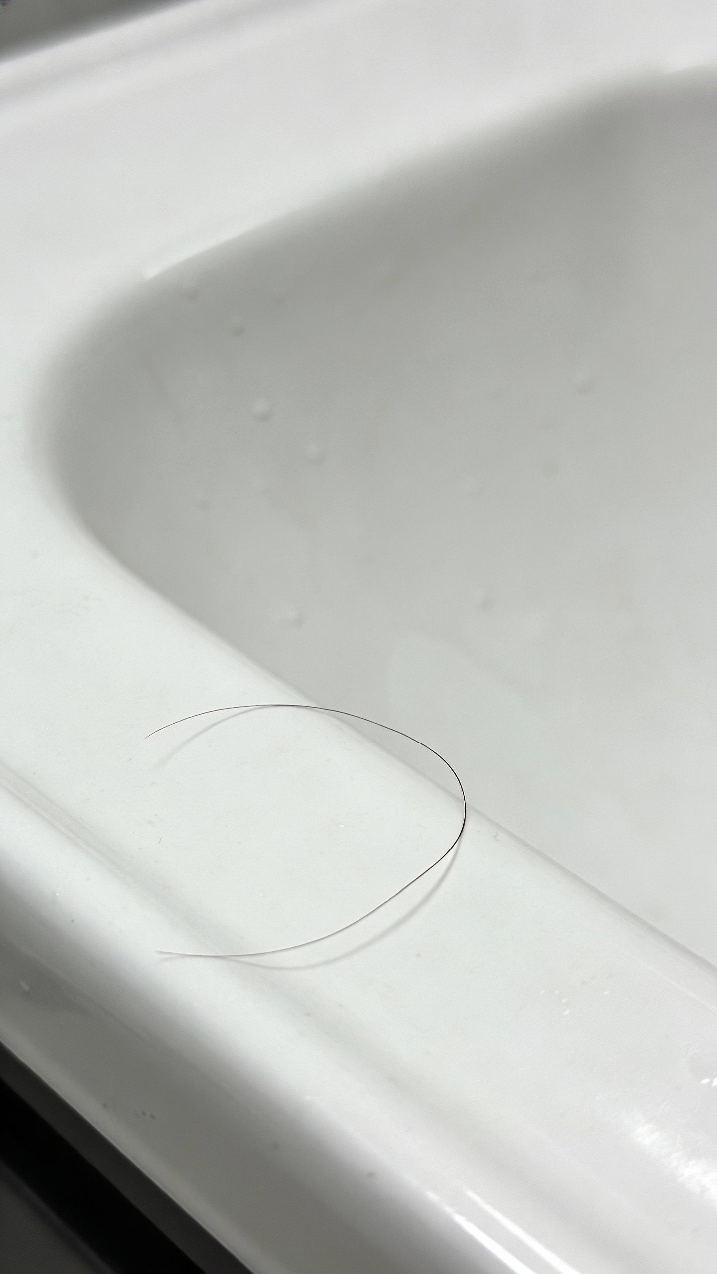 single strand of shed hair on white bathroom sink