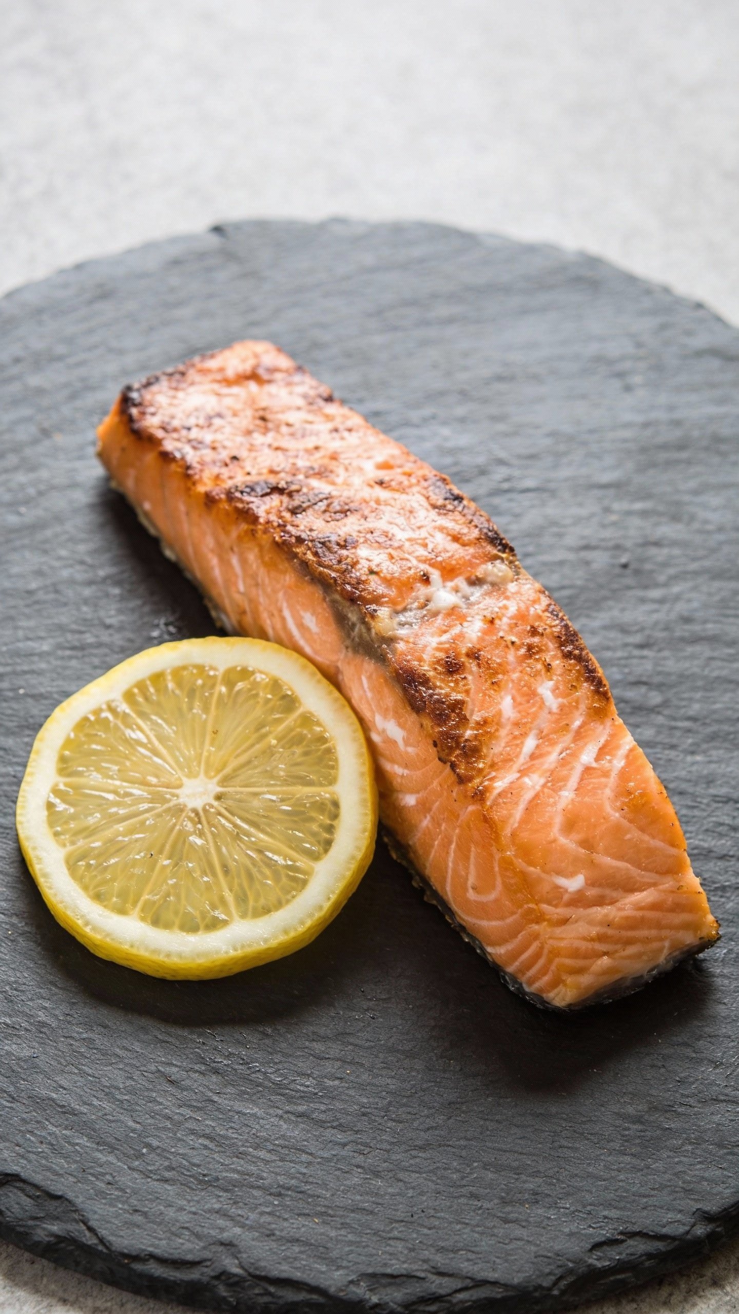 single salmon fillet with lemon on matte slate plate