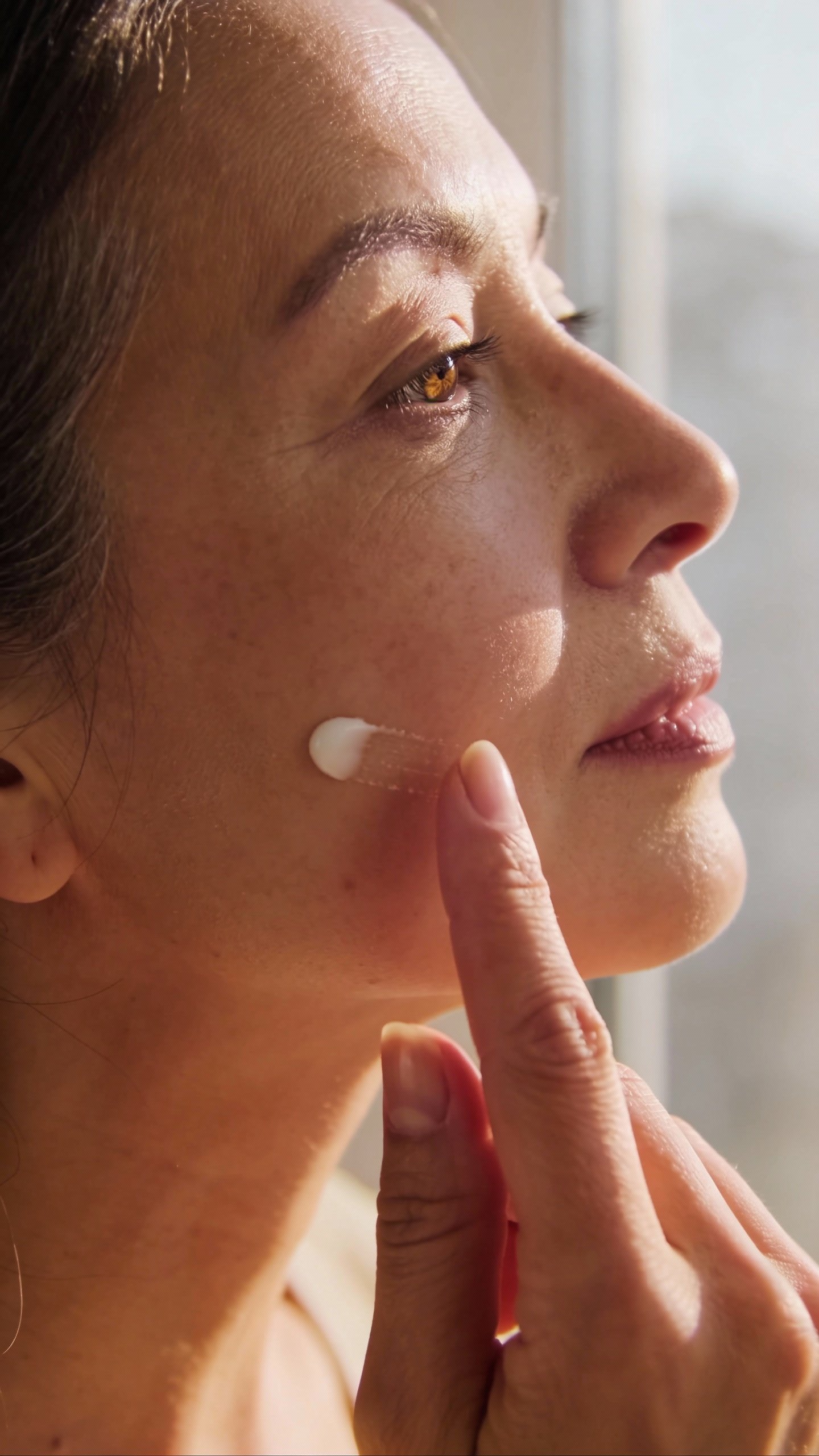 closeup of midlife woman applying ceramide cream, soft window light