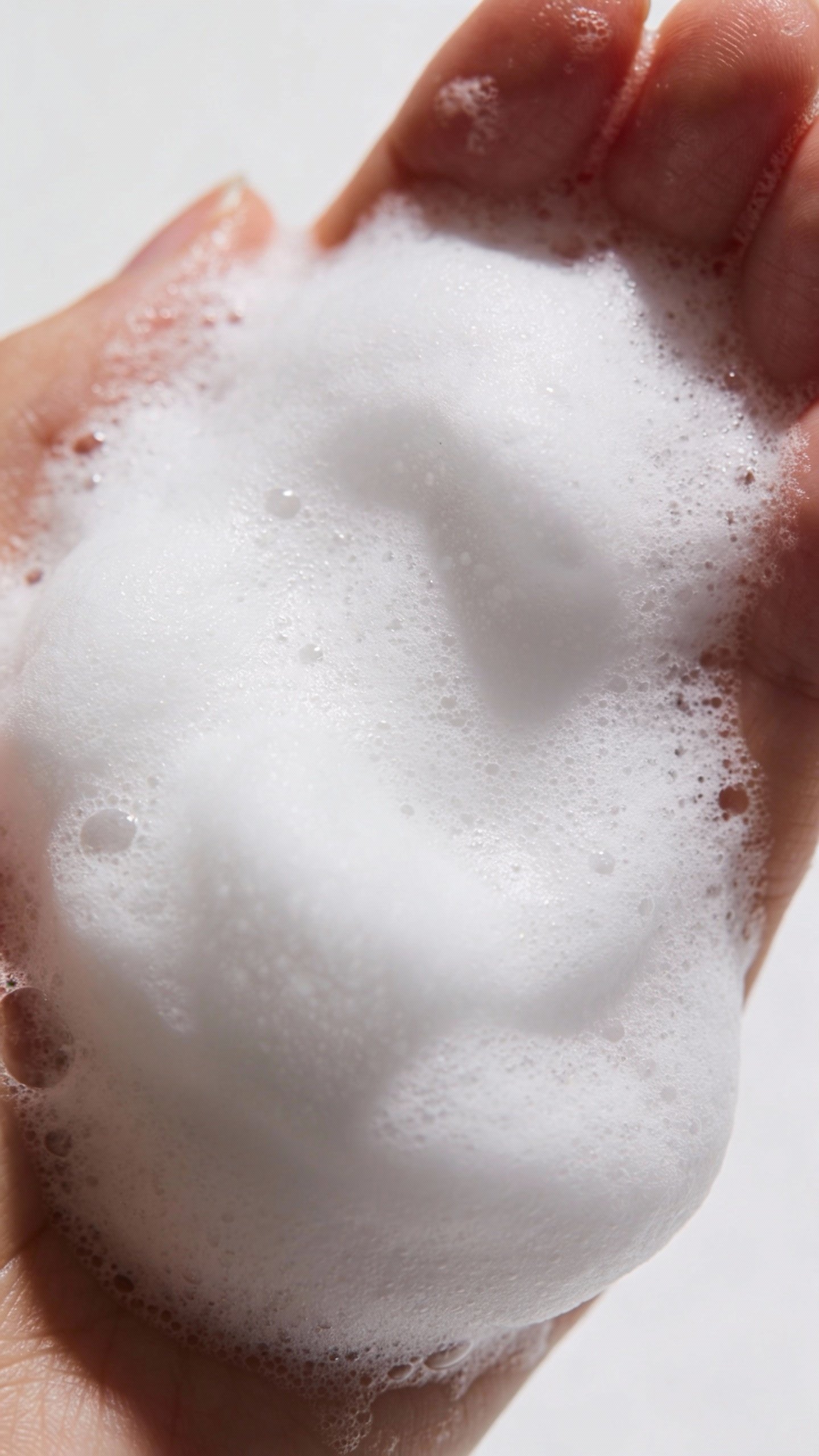 closeup of foaming salicylic acid cleanser in hand, minimal backdrop