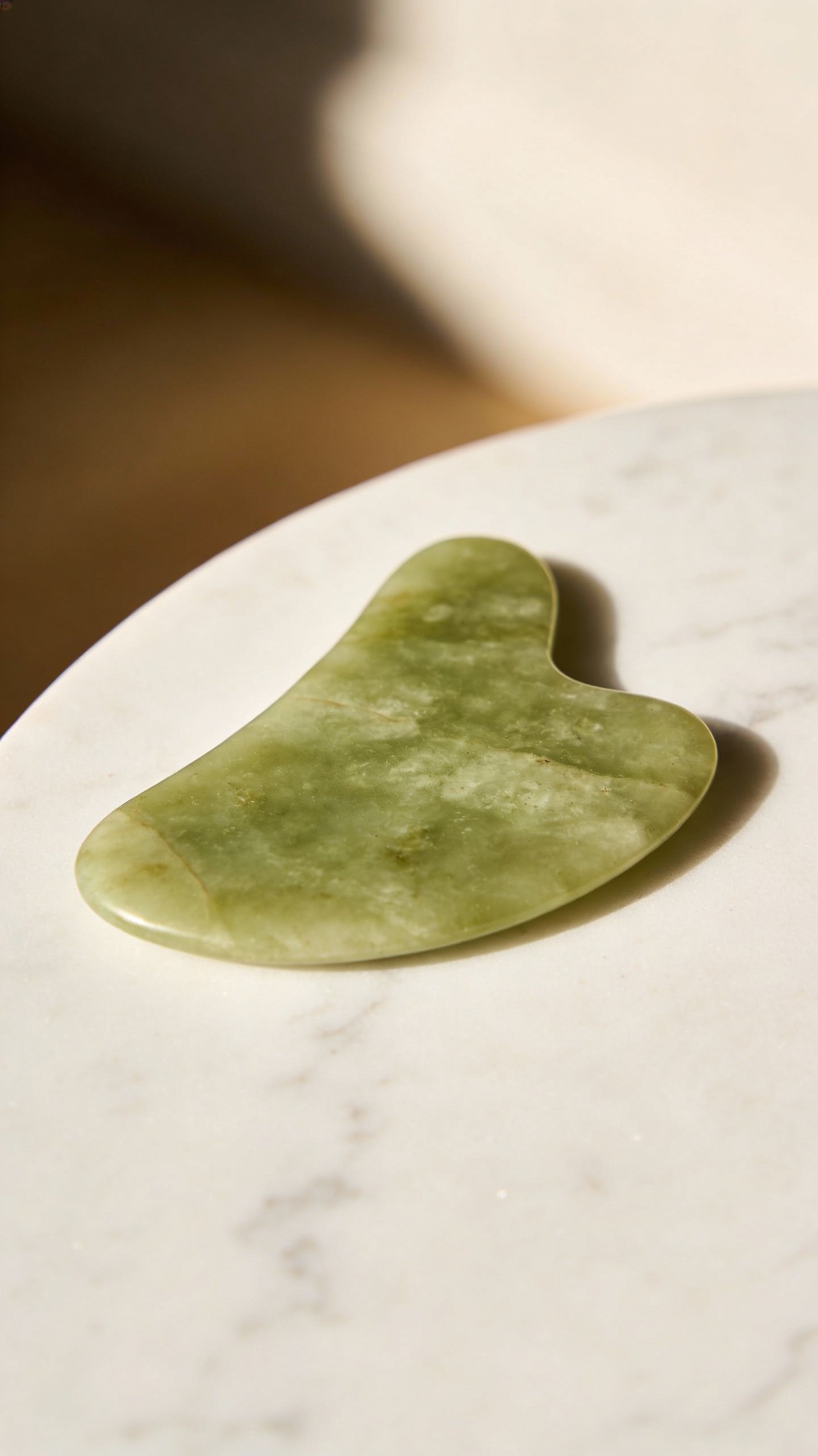 single jade gua sha on clean marble, soft studio light