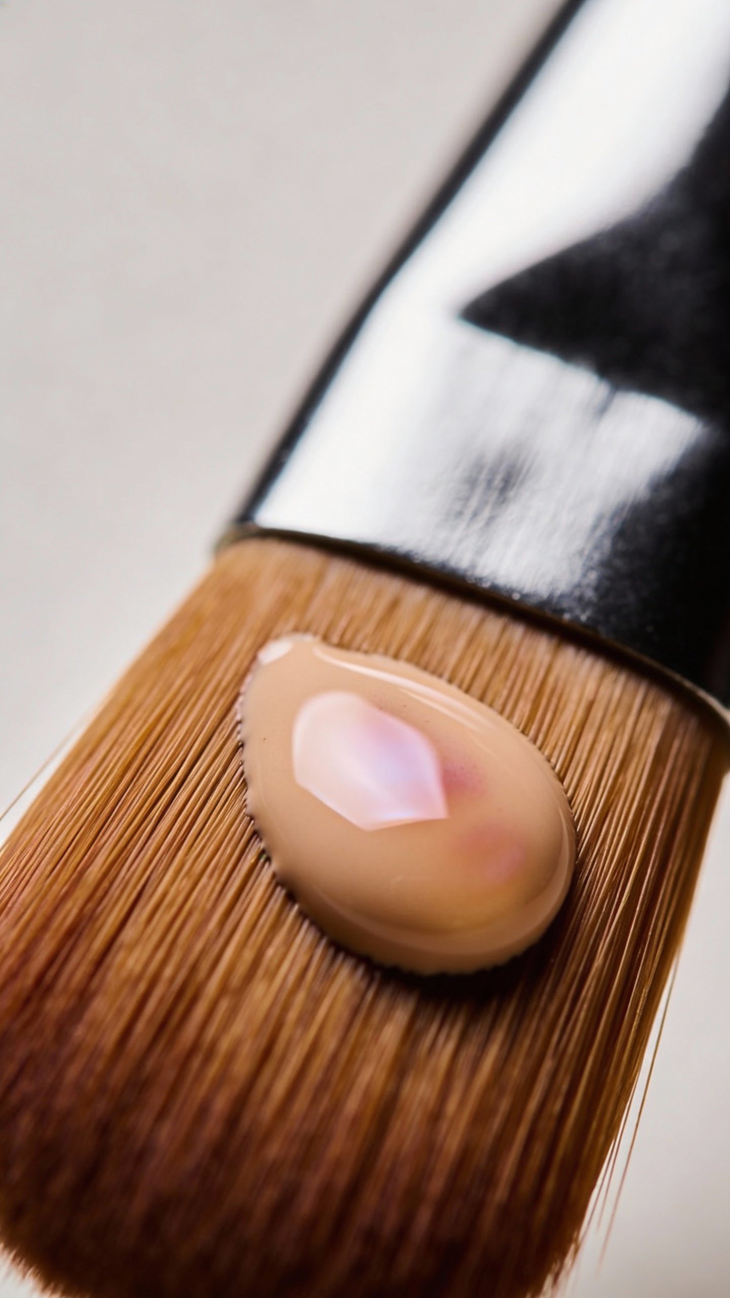Single foundation brush with tinted moisturizer drop, macro shot