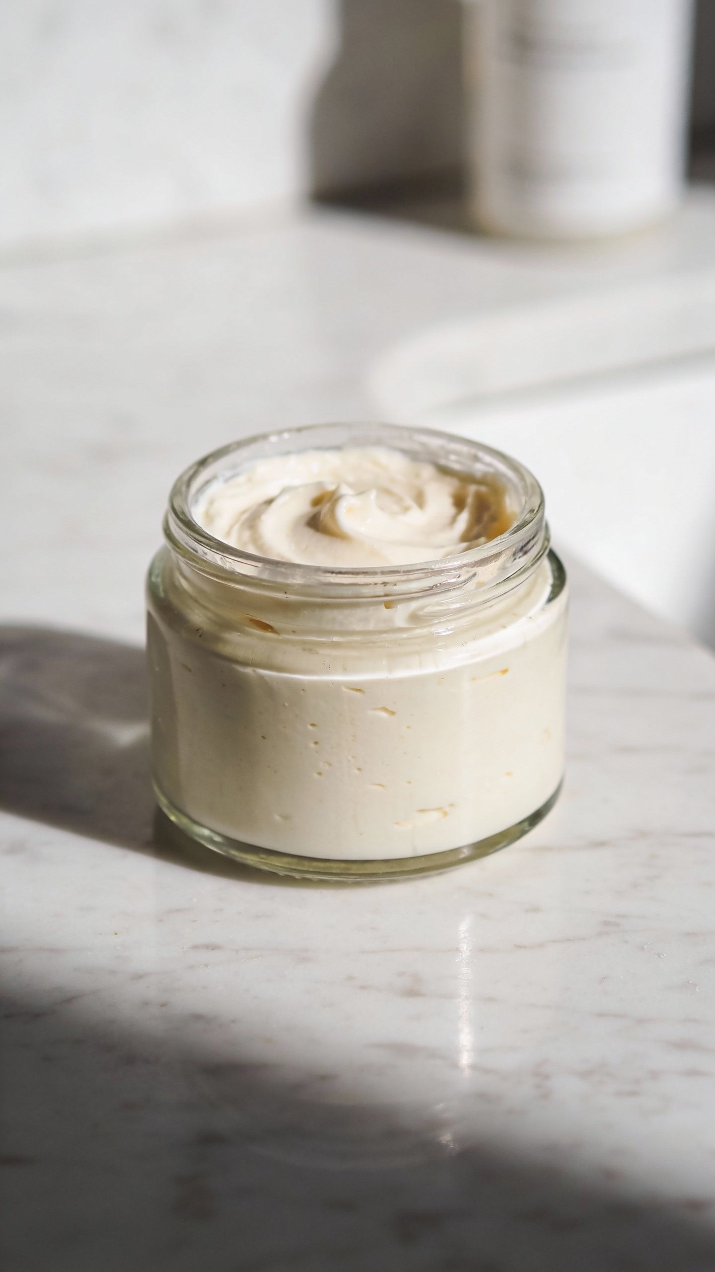 glass jar of diy face cream on white marble