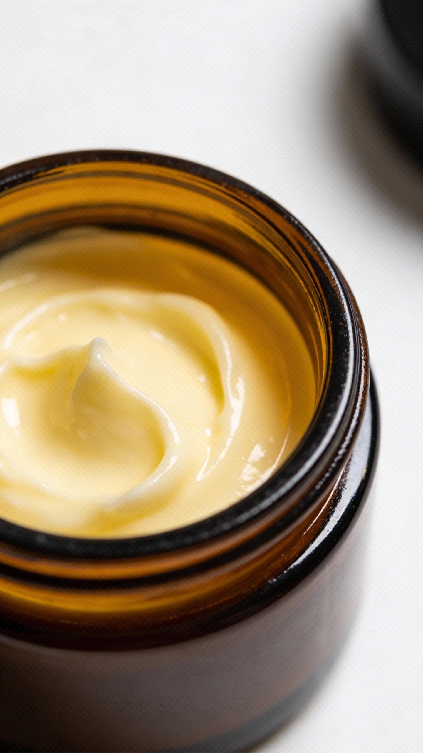 closeup amber glass jar of DIY face cream on white
