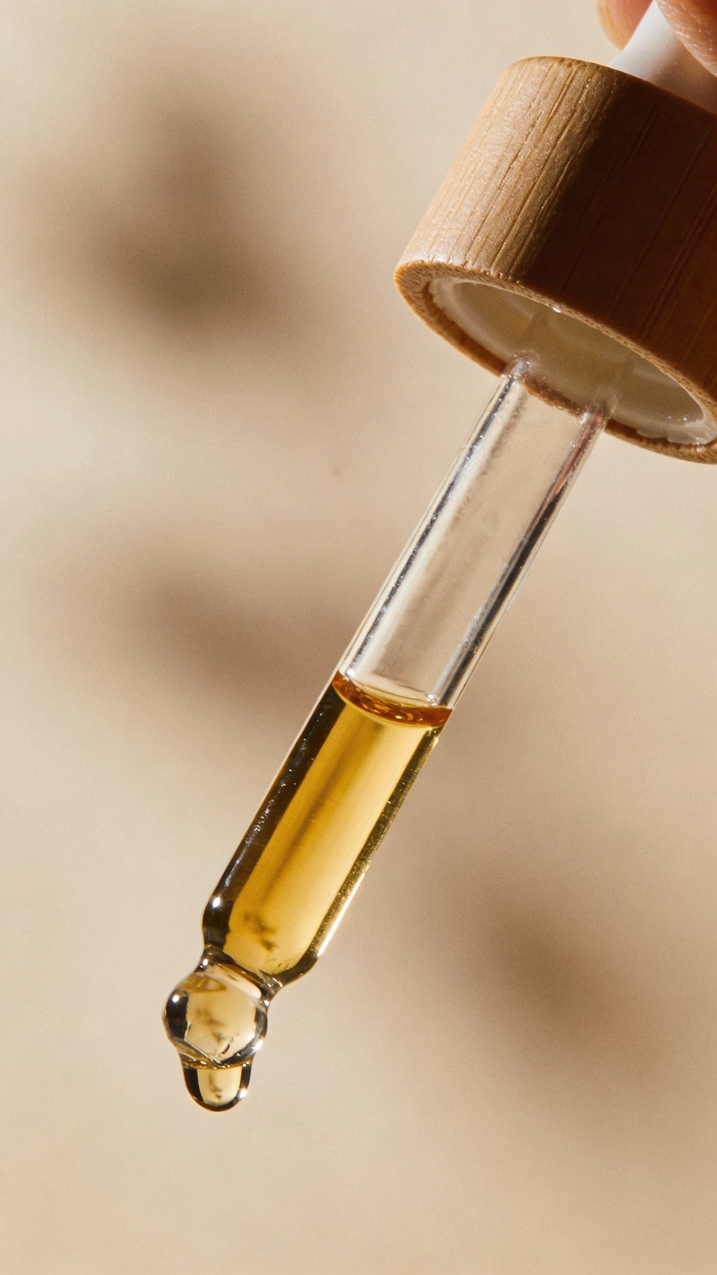single glass dropper of homemade facial oil against soft beige background