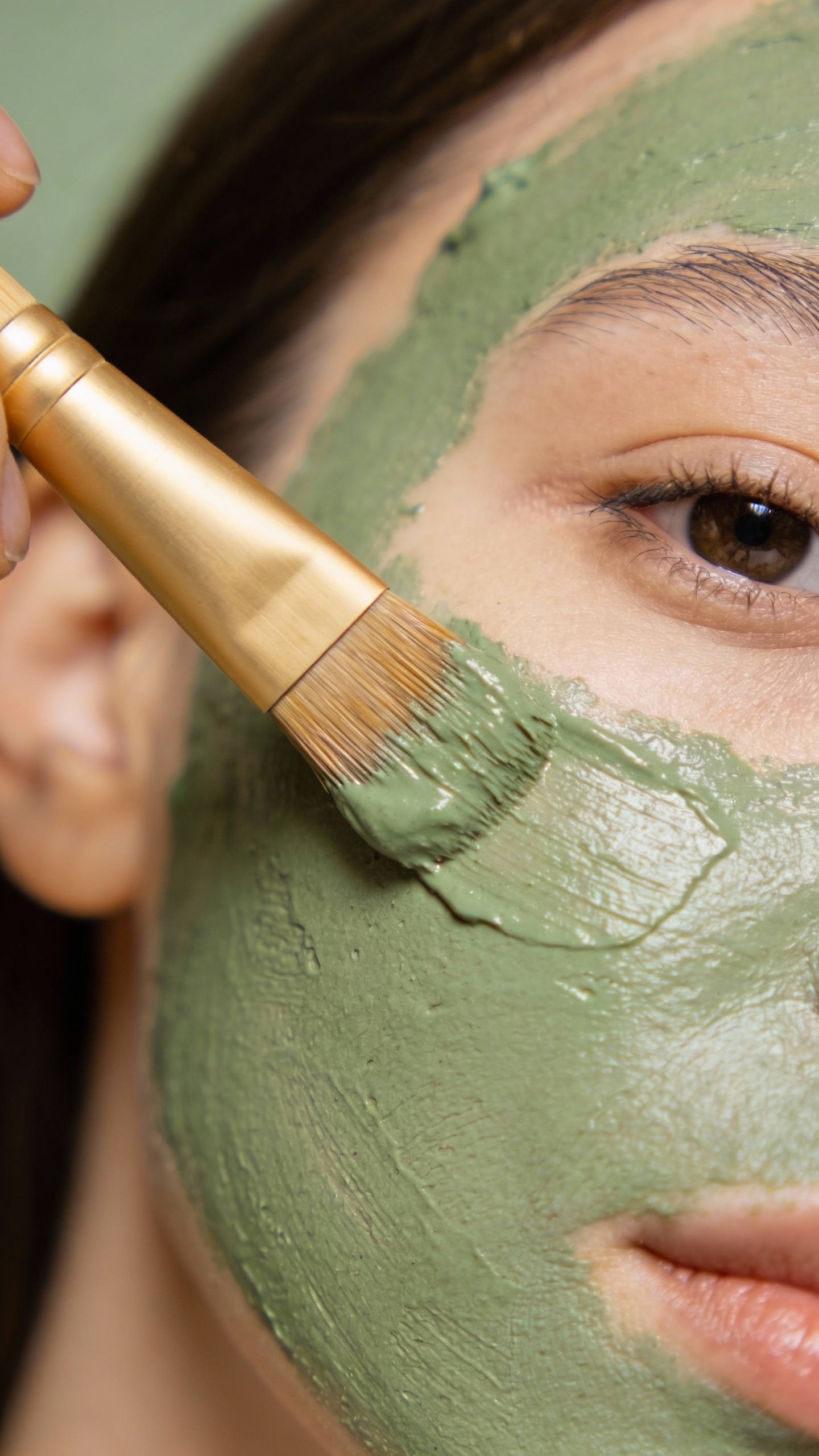 single bamboo brush applying green clay mask on cheek