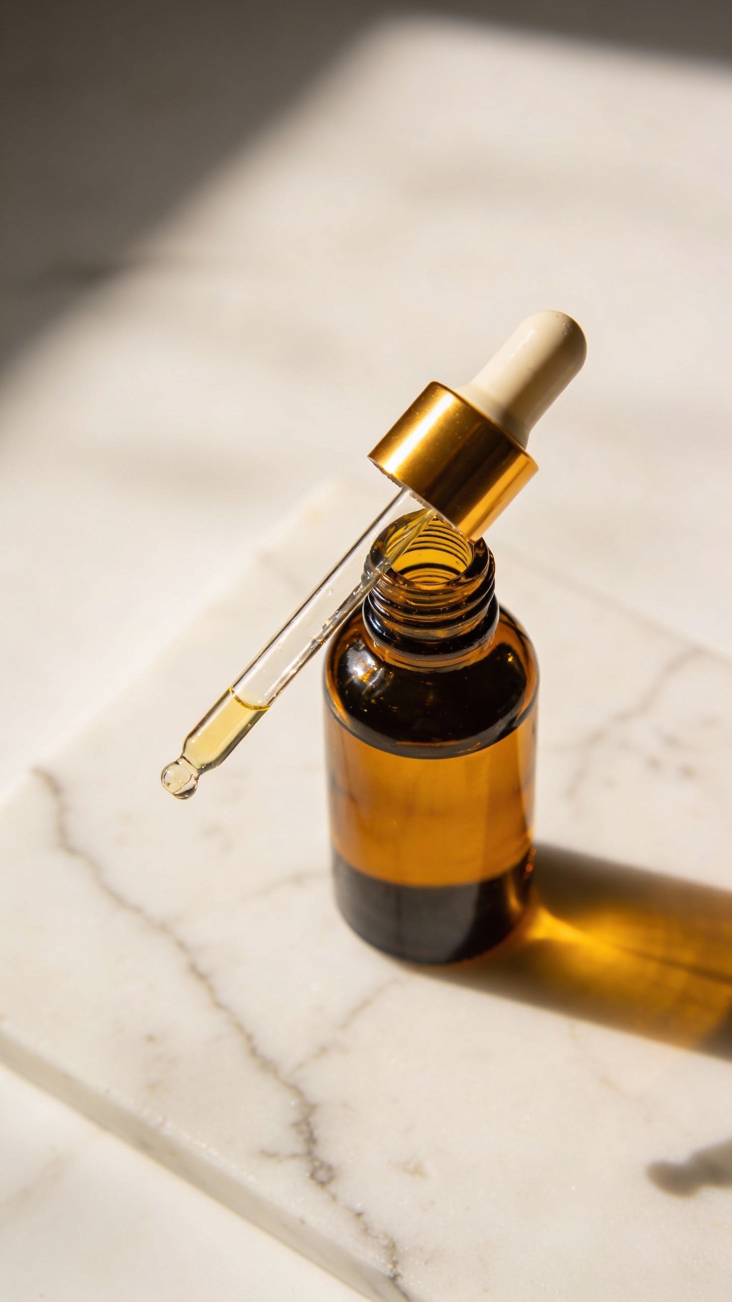 Amber glass dropper bottle of body oil on white marble