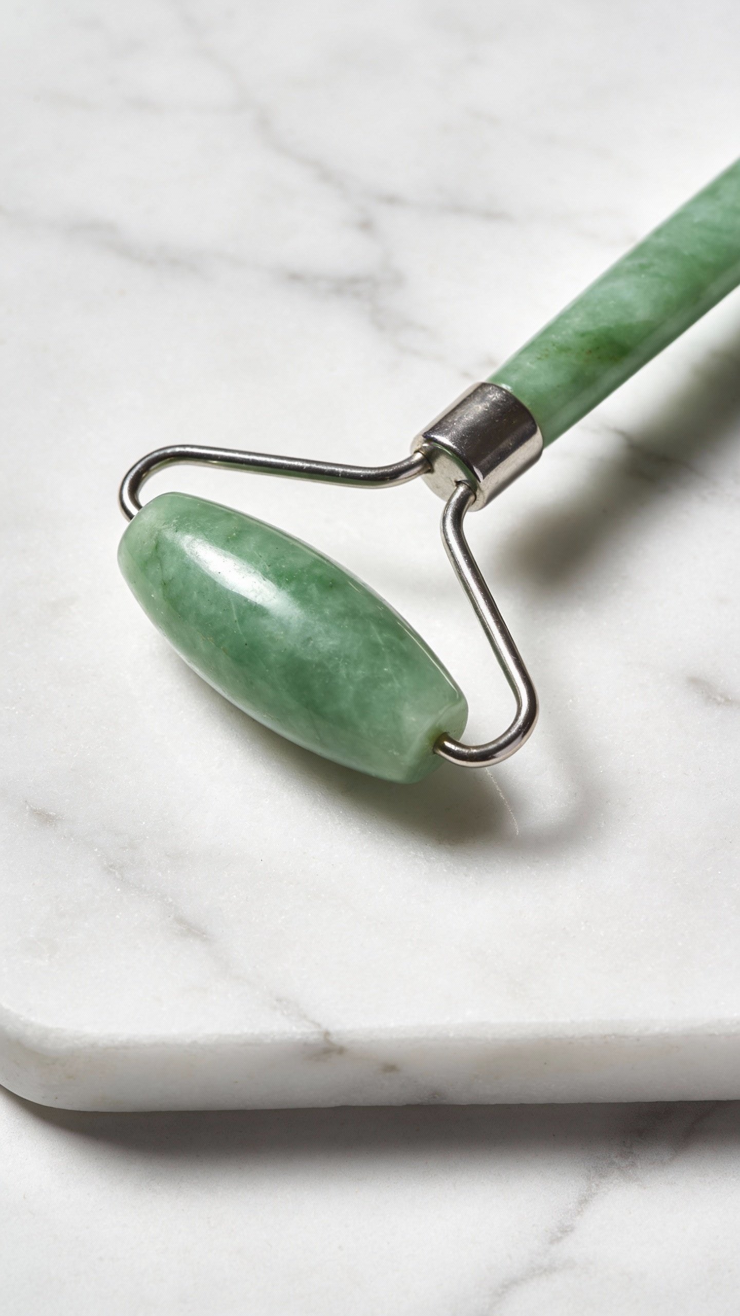 single jade roller on white marble, closeup