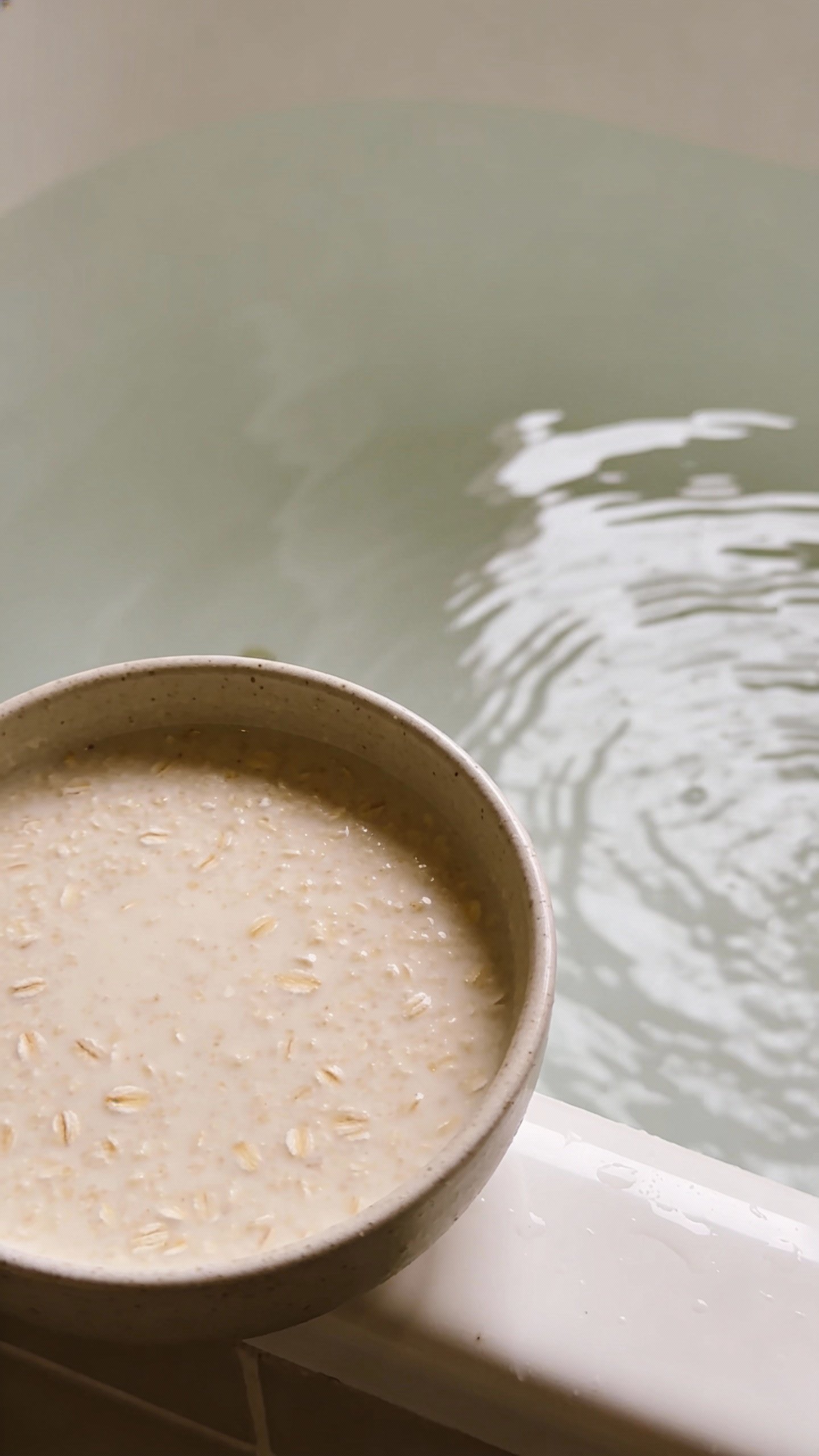 bowl of colloidal oatmeal beside lukewarm bathwater edge