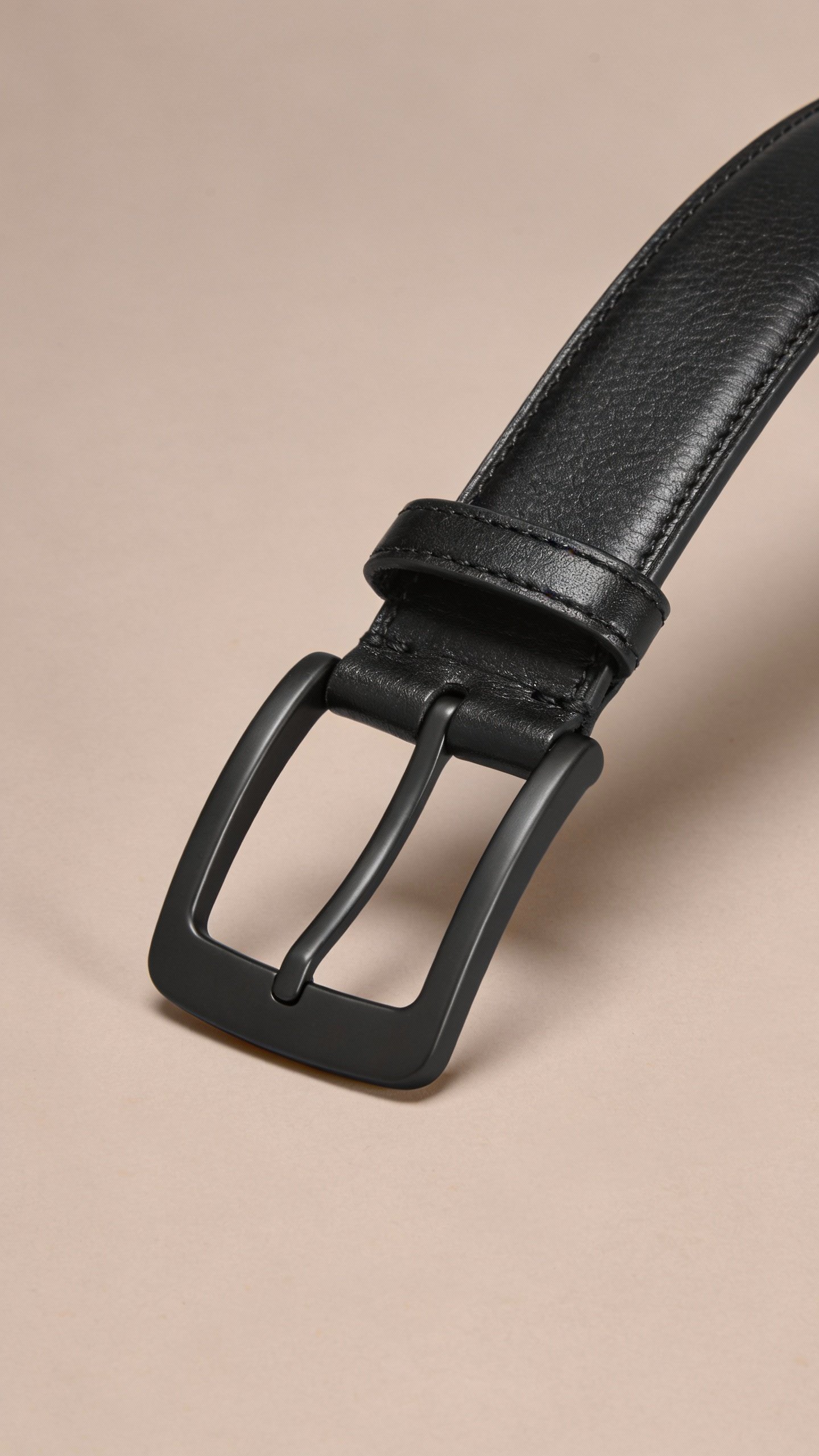 single black leather belt with matte buckle on neutral backdrop