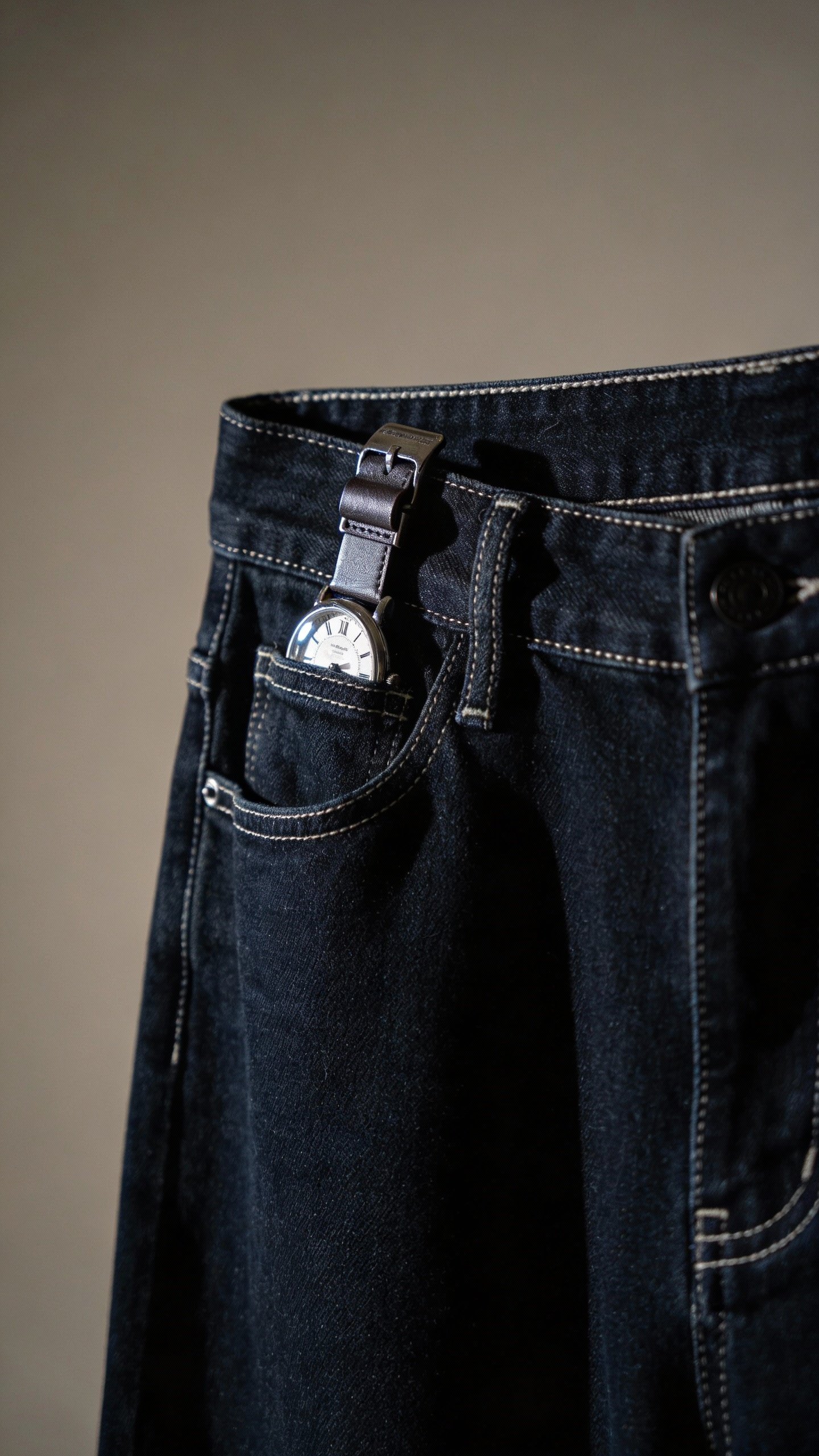 dark straight-leg jeans waistband with visible watch-clipped belt loop