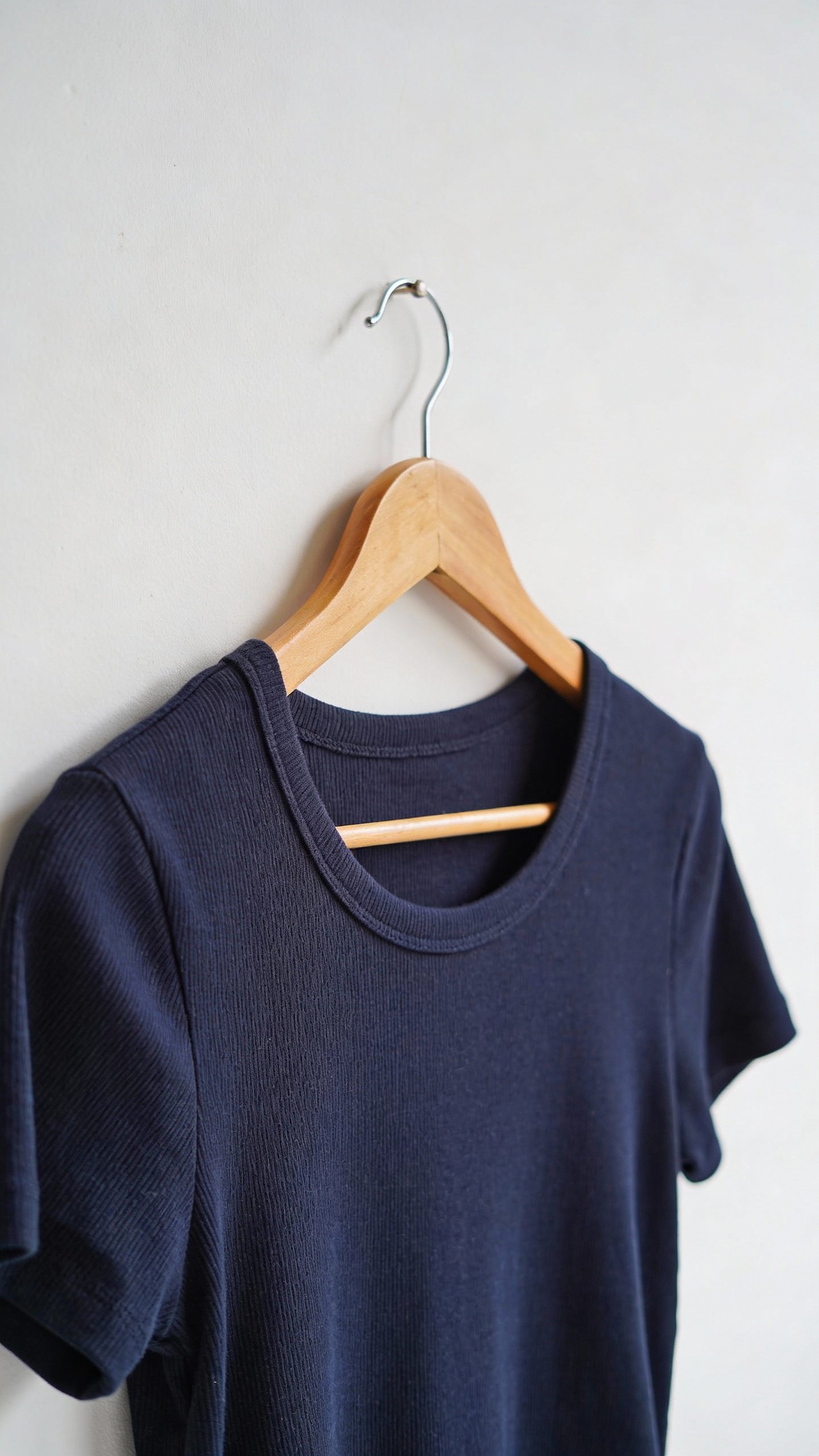 closeup navy knit tee on wooden hanger, white wall backdrop