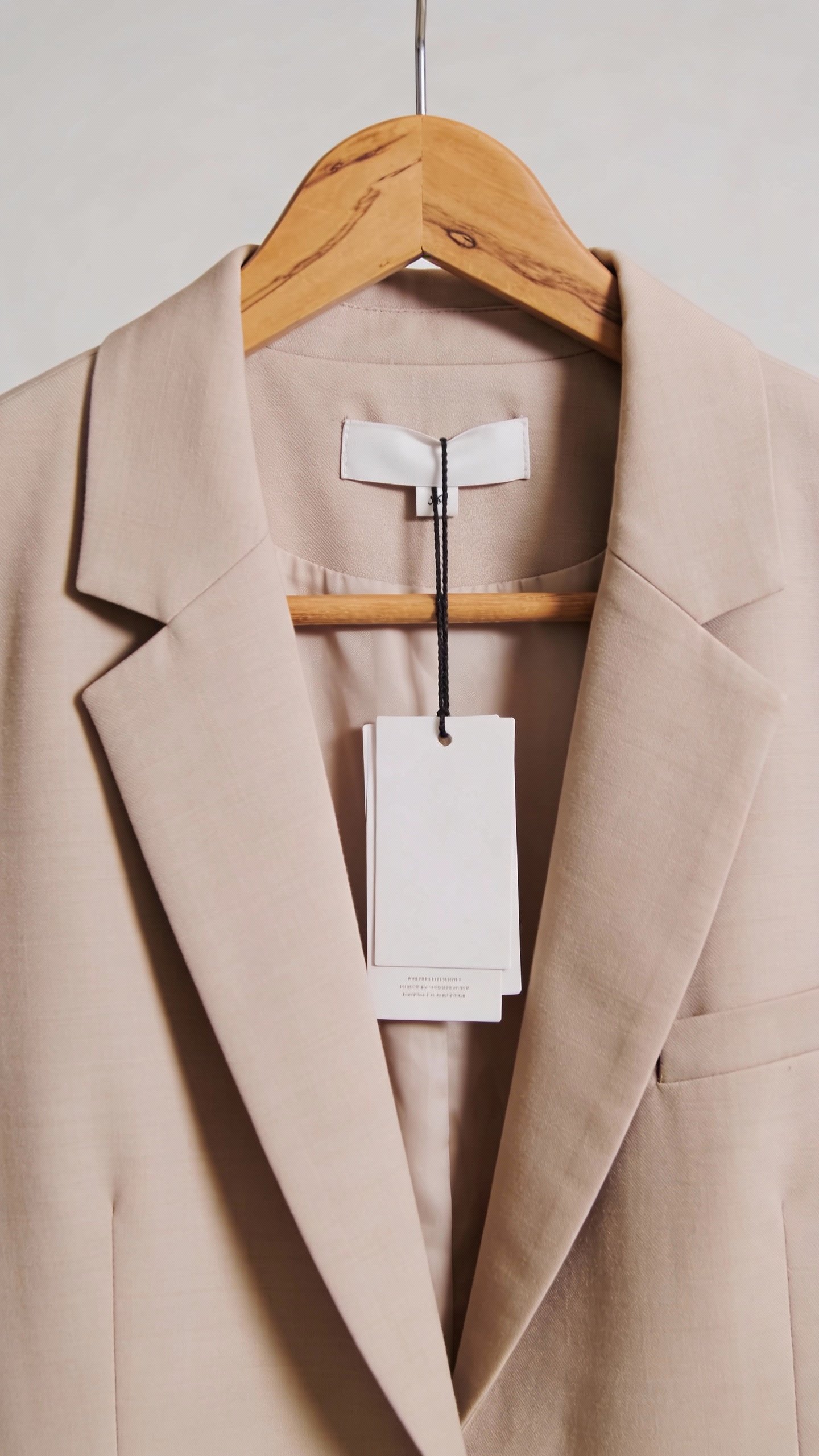 single neutral blazer on wooden hanger, tags attached
