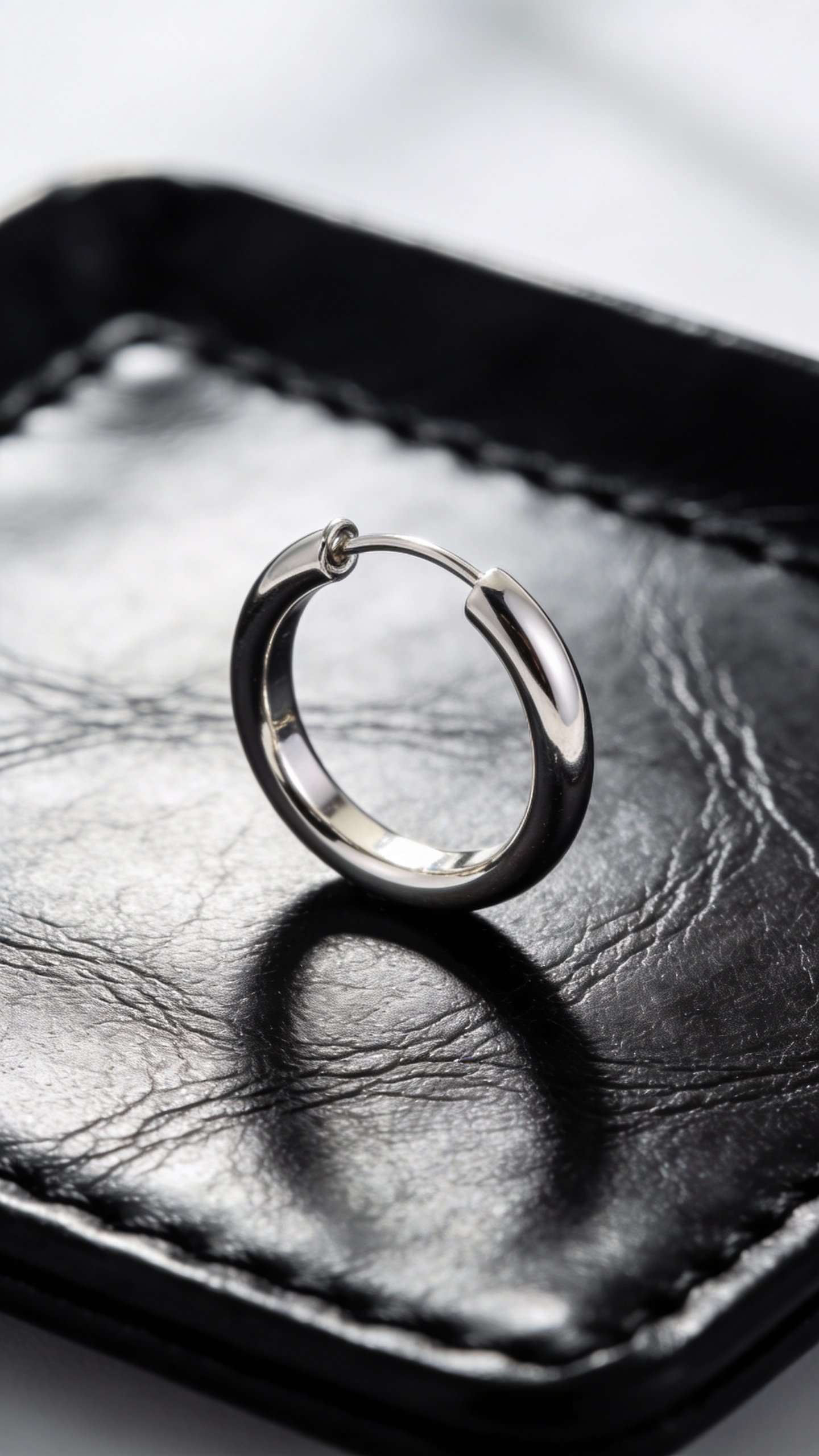 silver hoop earring on black leather tray, studio lighting