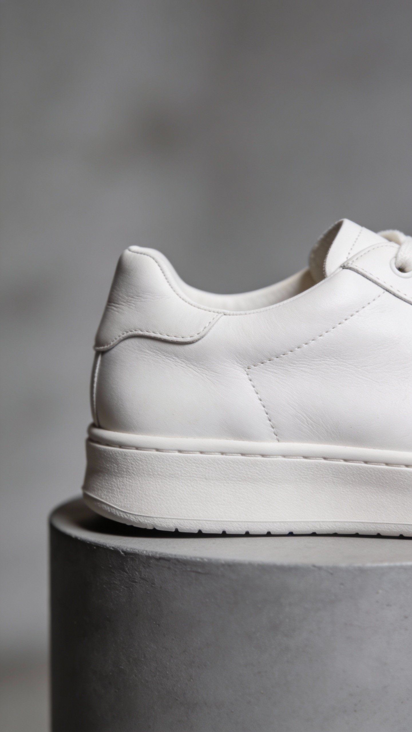 single white leather sneaker on gray pedestal, closeup