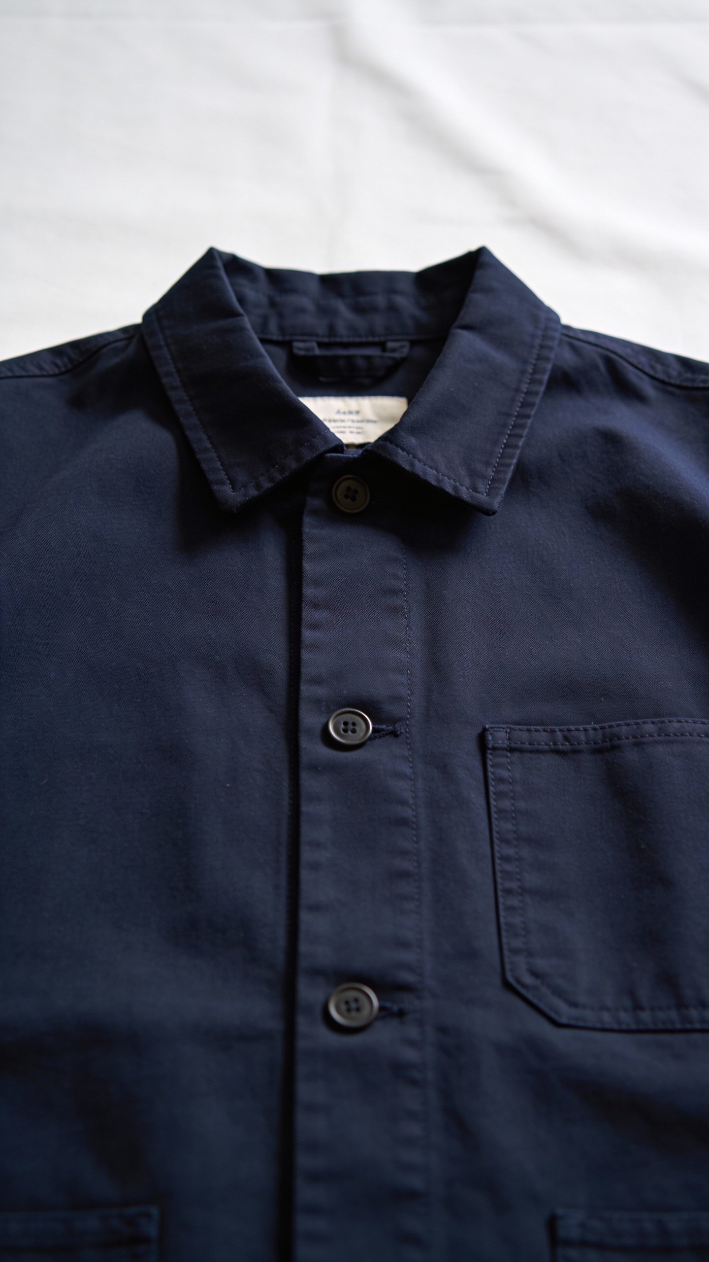 closeup of navy chore jacket on matte white backdrop