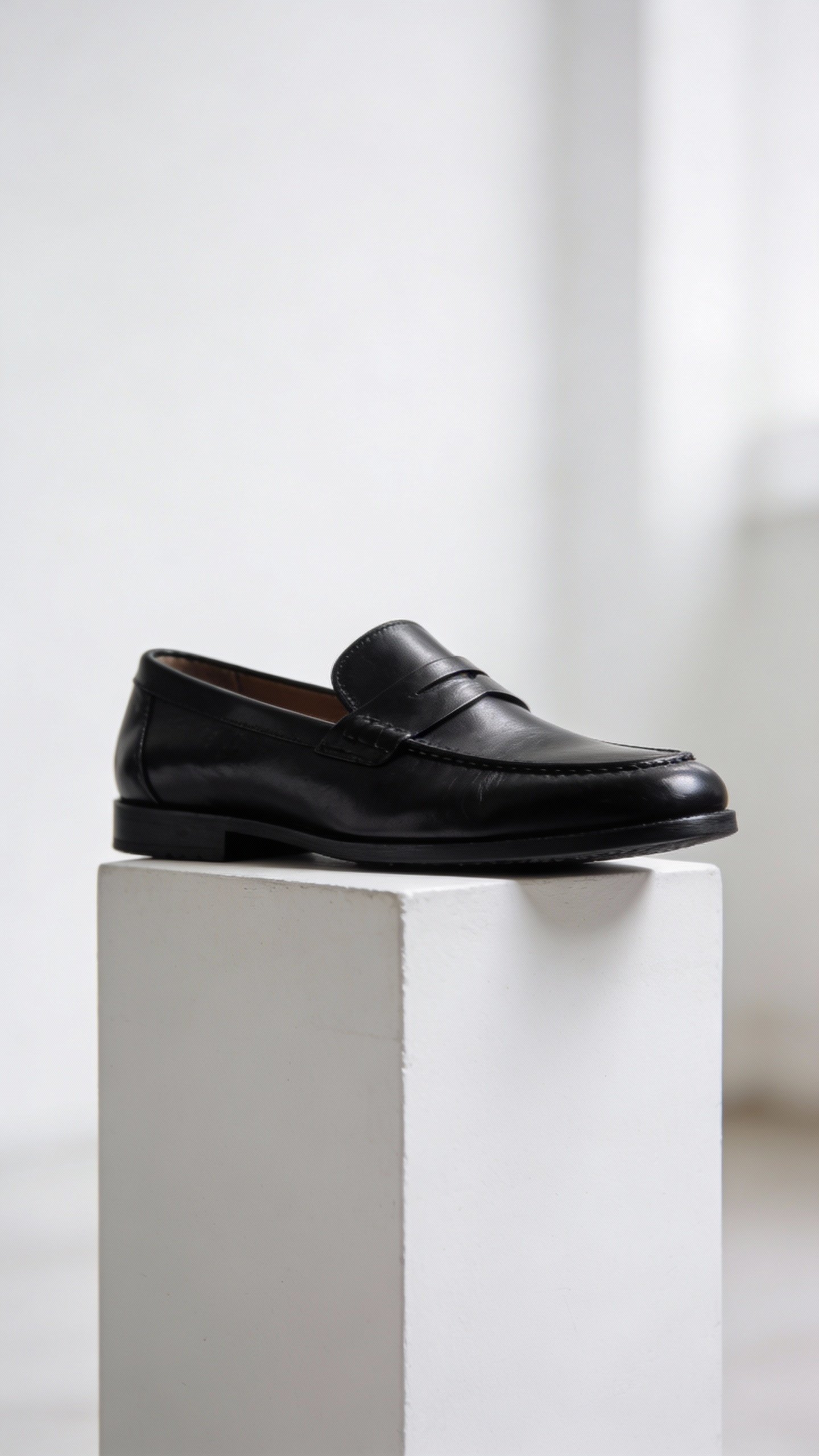 black leather loafer on white pedestal, studio lighting