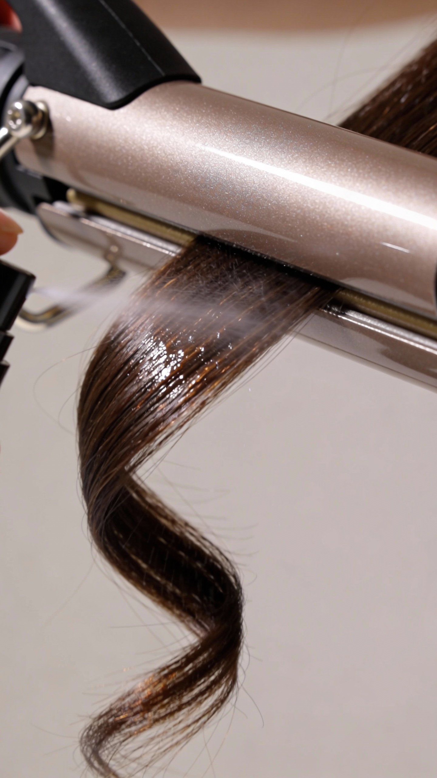 closeup of curling iron spraying heat protectant on strand